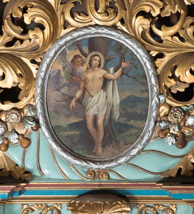 Zdjęcie nr 4: Obraz w formie stojącego owalu z przedstawieniem św. Sebastiana przywiązanego do drzewa. Święty ukazany jest w całej postaci, frontalnie, w kontrapoście. Lewą rękę ma uniesioną, prawą opadającą wzdłuż boku, obie przywiązane do gałęzi drzewa. Twarz ma okrągłą, o zamkniętych oczach i prostym nosie, okoloną krótkimi, brązowymi włosami. Wokół głowy nimb. Jego ciało jest umięśnione o rozbudowanej klatce piersiowej, w partii bioder przesłonięte białą tkaniną, której część zawieszona jest na drzewie po lewej stronie świętego. Po jego prawej widoczny nadlatujący na obłoku anioł, który wyciąga z jego boku strzałę. Scena ukazana jest na tle górzystego pejzażu. 