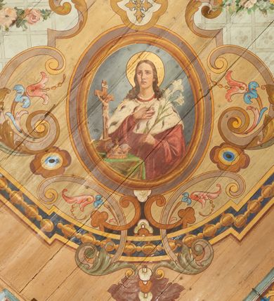 Zdjęcie nr 8: W prezbiterium w dolnej połowie ścian polichromia w formie namalowanej jasnoczerwonej, wielkowzorzytej tkaniny o motywach geometrycznych i roślinnych z niebieskim monogramem Marii i żółtymi koronami; jej górny brzeg odwiedziony jest pasem z brązowo-czerwoną dekoracją roślinną. Ściana przedzielona w połowie wysokości pasem z arkadkami wypełnionymi żółtymi wazonami oraz dekoracją roślinną na zielonym tle. W ich przyłuczach czerwone pola wypełnione malowaną roślinnością. W górnej połowie ścian malowane płyciny o jasnobrązowych ramach, których pola wypełnione są wzorem o motywie żółtych sześcioboków z fioletowymi kwiatami. Na południowej ścianie prezbiterium okna obwiedzione malowanymi, mazerowanymi ramami. W górnej części ściany, pod belkowaniem fryz utworzony z uskrzydlonych główek anielskich ukazanych na niebieskim tle, pomiędzy którymi znajdują się czerwone kampanule, pod nim podwieszone kwiatowe girlandy. Ściany zakończone profilowanym gzymsem, pomalowanym w dwa pasy – czerwony i niebieski, dekorowane motywem liści. Ściany podzielone lizenami w kolorze fioletowym, zdobionymi motywami geometrycznymi, różnymi w dolnej i górnej połowie. Strop prezbiterium z namalowaną płyciną w formie stojącego prostokąta, zamkniętego u dołu trójbocznie, o wklęsłych sześciu narożach, w których namalowana jest dekoracja roślinna. Płycina ujęta brązowo-żółtą ramą zdobioną motywem roślinnym oraz niebieskim pasem, z abstrakcyjnym motywem na wklęśnięciach. Różowe pole wypełnione białą kratką z kwiatami. W jego centrum owalny medalion w malowanej, profilowanej ramie oraz niebieskiej opasce z wypustkami, na których zawieszonych jest wokół osiem kwiatowych girland oraz cztery fantazyjne motywy kwiatowe. W medalionie namalowana scena Koronacji Matki Bożej. W jego centrum siedząca na obłokach Maria, ukazana frontalnie, z prawą ręką złożoną na piersi, lewą wyciągniętą w bok. Twarz ma pociągłą, o migdałowatych oczach, prostym nosie i pełnych ustach, okoloną długimi, falowanymi, jasnymi włosami. Ubrana jest w białą tunikę i niebieski płaszcz zarzucony na ramiona i kolana. Po jej prawej siedzi Chrystus, zwrócony w trzech czwartych w lewo, pochylony, prawą ręką podtrzymuje nad jej głową koronę. Twarz ma podłużną, o okrągłych oczach, lekko garbatym nosie i pełnych ustach, okolona brązowymi włosami i brodą. Ubrany jest w białą tunikę i czerwony płaszcz, o jego lewe ramię oparty jest krzyż. Po lewej stronie Marii siedzi Bóg Ojciec, zwrócony w trzech czwartych w prawo, lewą ręką przytrzymuje przy boku kulę, prawą podtrzymuje koronę nad głową Marii. Bóg ukazany jako starzec, o wysokim czole, podłużnej twarzy, małych oczach, garbatym nosie i pełnych ustach. Włosy i brodę ma długie i siwe. Ubrany jest w fioletową tunikę i jasnobrązowy płaszcz. Nad postaciami unosi się gołębica Ducha Świętego w glorii promienistej. Scena ukazana na tle błękitnego nieba, wypełnionego obłokami, w dolnej części obrazu z ukazanymi uskrzydlonymi główkami anielskimi. 
Ściany nawy w jednej trzeciej wysokości obwiedzione są pasem z malowanymi czerwono-brązowymi płycinami o naprzemiennym układzie owali i rombów, wypełnionymi dekoracją geometryczną i motywami roślinnymi. Ponad nimi wzdłuż ściany malowany niebieski pas o kolorowej i fantazyjnej dekoracji. Ściany w dwóch trzecich wysokości pokryte jasnoróżową polichromią o wielobarwnym, fantazyjnym, geometryczno-roślinnym wzorze z motywem równoramiennych krzyży. Ściany zakończone niebieskim fryzem przypominającym lambrekin z motywami geometrycznymi. Całość opasana profilowanym gzymsem, pomalowanym w dwa pasy – czerwony i niebieski, z dekoracją o motywach liści. Ściany podzielone lizenami pomalowanymi na kolor fioletowy, z dekoracją geometryczną. Na ścianach północnej i południowej po dwa okna obwiedzione malowanymi, mazerowanymi ramami. Pomiędzy oknami sceny w formie stojącego prostokąta zamkniętego łukiem półkolistym, w malowanej ramie dekorowanej cekinami. U dołu ramy fragment gzymsu dekorowanego kimationem z podwieszeniem zdobionym uskrzydloną główką anielską i meandrem. Rama zamknięta gzymsem wyłamanym na kształt łuku odcinkowego, podtrzymywanym na konsolach, dekorowanych motywem roślinnym. 
Na ścianie północnej scena z przedstawieniem św. Jakuba Większego z aniołem. W dolnej części obrazu święty w pozycji półleżącej, oparty o schody, ukazany frontalnie, z uniesioną głową, skierowaną w lewo i skrzyżowanymi na piersi rekami. Twarz ma owalną, o dużych oczach skierowanych w górę, prostym nosie i rozchylonych ustach, okoloną, krótkimi, jasnobrązowymi włosami i brodą. Wokół jego głowy nimb. Ubrany jest w ciemnobrązową tunikę, przepasaną sznurem, na lewym ramieniu ma muszlę, lewą ręką przytrzymuje laskę z bukłakiem. Na stopach ma sandały. Nad świętym unosi się anioł, zwrócony w trzech czwartych w lewo, w wykroku, z pochyloną głową, w prawej ręce trzyma liść palmy, w lewej, nad głową świętego - wieniec z róż. Anioł o młodzieńczej twarzy, z dużymi oczami zwróconymi w dół, dużym nosem i małymi ustami, okolonej jasnymi włosami sięgającymi ramion. Ubrany jest w żółtą tunikę oraz jasnofioletowy płaszcz. Ma białe i rozłożone skrzydła. Ukazany jest w otoczeniu obłoków. Poniżej, obok świętego na ziemi leży puklerz i miecz. Postacie ukazane we wnętrzu, z widoczną murowaną ścianą z oknami, fragmentem kolumny i schodami. W prawym dolnym sygnatura „M. Szczurowsk[i]”. 
Na ścianie południowej scena z przedstawieniem św. Izydora Oracza modlącego się przed kapliczką. W dolnej części obrazu święty w pozycji klęczącej, zwrócony profilem w prawo, z uniesionymi rękami o splecionych dłoniach w geście modlitwy, z uniesioną głową. Twarz ma szczupłą, o oczach skierowanych w górę, małym nosie i pełnych ustach, okoloną krótkimi, brązowymi włosami. Ubrany jest w białą koszulę, niebieski kaftan z czerwoną podszewką, przepasany w talii, z zawieszonym kluczem, na stopach ma buty. Przed nim, na ziemi leżą słomkowy kapelusz i bat. Przed świętym kapliczka w formie kamiennego krucyfiksu na cokole, pośród krzaków z kwiatami. Święty ukazany na tle pejzażu, z widocznym w oddali polem, na którym dwa woły ciągną pług, prowadzony przez anioła. Powyżej błękitne niebo zasnute ciemnymi chmurami, spod których wydobywa się strumień światła. W prawym dolnym rogu sygnatura „M. Szczurowski”. 
W zachodniej części nawy beżowa balustrada chóru muzycznego, na której namalowane są prostokątne płyciny, o krótszych bokach dekorowanych motywem roślinnym. Ich pola wypełnia niebieska opaska oraz różowa kratka ze zdobieniem roślinnym. Płycina środkowa w formie owalu z przedstawieniem Dawida, siedzącego na tronie i grającego na harfie. Postać ukazana do połowy, zwrócona w trzech czwartych w prawo, dwiema wyciągniętymi rękami dotyka strun harfy. Dawid o pociągłej twarzy, ze schematycznie oddanymi rysami, okolony brązowymi włosami i brodą. Na głowie ma koronę otwartą. Ubrany jest w czerwoną suknię, na ramiona ma narzuconą gronostajową pelerynę. Nad nim zawieszony czerwony baldachim, z zieloną podszewką. W oddali widoczny zarys zabudowań miejskich. Profile cokołu i gzymsu balustrady malowane w kolorowe pasy, z dekoracją roślinną. 
Na stropie nawy malowana płycina w formie stojącego prostokąta o zaokrąglonych narożach, ujęta niebieską ramą o geometrycznym wzorze, w miejscu naroży stylizowane roślinne palmety. W narożach płyciny cztery owalne medaliony z popiersiami św. Stanisława Kostki, św. Kazimierza Jagiellończyka, św. Stanisława z Piotrowinem i św. Jana Kantego. Medaliony ujęte są wolutowymi kartuszami, dekorowanymi stylizowanym ornamentem roślinnym. W polu centralnym malowanej płyciny scena ze św. Klemensem w formie stojącego prostokąta o wklęsłych narożach, ujęta malowaną ramą, w narożach uskrzydlone główki anielskie. Scena otoczona drugą ramą o fantazyjnym zarysie, dekorowaną na bokach fantazyjnymi szczytami z ornamentem roślinnym, które połączone są kwiecistymi girlandami z narożnymi kartuszami. Scena ze św. Klemensem przedstawia go w kamieniołomie, błogosławiącego robotników z kilofami. Święty ukazany jest jako starzec, z siwą brodą i włosami oraz łysiną na głowie. Ubrany jest w jasnofioletową sutannę, białą rokietę z dekoracyjnym obszyciem oraz jasnoczerwony, szeroki ornat, na piersi ma paliusz. W tle pomiędzy dwoma wzniesieniami skalnymi widoczne morze, z płynącym statkiem, w oddali zaś brzeg z domem. Na skarpie w lewej części obrazu ukazany baranek w glorii promienistej, na przeciwległej dwaj żołnierze, którzy zrzucili świętego z kotwicą zawieszoną u szyi do morza. Przy dolnej krawędzi obrazu sygnatura „pinxit 1910 / M. Szczurowski”.
