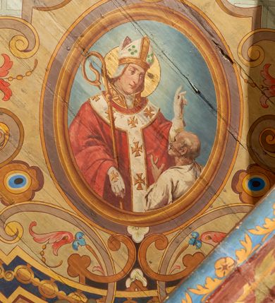 Zdjęcie nr 10: W prezbiterium w dolnej połowie ścian polichromia w formie namalowanej jasnoczerwonej, wielkowzorzytej tkaniny o motywach geometrycznych i roślinnych z niebieskim monogramem Marii i żółtymi koronami; jej górny brzeg odwiedziony jest pasem z brązowo-czerwoną dekoracją roślinną. Ściana przedzielona w połowie wysokości pasem z arkadkami wypełnionymi żółtymi wazonami oraz dekoracją roślinną na zielonym tle. W ich przyłuczach czerwone pola wypełnione malowaną roślinnością. W górnej połowie ścian malowane płyciny o jasnobrązowych ramach, których pola wypełnione są wzorem o motywie żółtych sześcioboków z fioletowymi kwiatami. Na południowej ścianie prezbiterium okna obwiedzione malowanymi, mazerowanymi ramami. W górnej części ściany, pod belkowaniem fryz utworzony z uskrzydlonych główek anielskich ukazanych na niebieskim tle, pomiędzy którymi znajdują się czerwone kampanule, pod nim podwieszone kwiatowe girlandy. Ściany zakończone profilowanym gzymsem, pomalowanym w dwa pasy – czerwony i niebieski, dekorowane motywem liści. Ściany podzielone lizenami w kolorze fioletowym, zdobionymi motywami geometrycznymi, różnymi w dolnej i górnej połowie. Strop prezbiterium z namalowaną płyciną w formie stojącego prostokąta, zamkniętego u dołu trójbocznie, o wklęsłych sześciu narożach, w których namalowana jest dekoracja roślinna. Płycina ujęta brązowo-żółtą ramą zdobioną motywem roślinnym oraz niebieskim pasem, z abstrakcyjnym motywem na wklęśnięciach. Różowe pole wypełnione białą kratką z kwiatami. W jego centrum owalny medalion w malowanej, profilowanej ramie oraz niebieskiej opasce z wypustkami, na których zawieszonych jest wokół osiem kwiatowych girland oraz cztery fantazyjne motywy kwiatowe. W medalionie namalowana scena Koronacji Matki Bożej. W jego centrum siedząca na obłokach Maria, ukazana frontalnie, z prawą ręką złożoną na piersi, lewą wyciągniętą w bok. Twarz ma pociągłą, o migdałowatych oczach, prostym nosie i pełnych ustach, okoloną długimi, falowanymi, jasnymi włosami. Ubrana jest w białą tunikę i niebieski płaszcz zarzucony na ramiona i kolana. Po jej prawej siedzi Chrystus, zwrócony w trzech czwartych w lewo, pochylony, prawą ręką podtrzymuje nad jej głową koronę. Twarz ma podłużną, o okrągłych oczach, lekko garbatym nosie i pełnych ustach, okolona brązowymi włosami i brodą. Ubrany jest w białą tunikę i czerwony płaszcz, o jego lewe ramię oparty jest krzyż. Po lewej stronie Marii siedzi Bóg Ojciec, zwrócony w trzech czwartych w prawo, lewą ręką przytrzymuje przy boku kulę, prawą podtrzymuje koronę nad głową Marii. Bóg ukazany jako starzec, o wysokim czole, podłużnej twarzy, małych oczach, garbatym nosie i pełnych ustach. Włosy i brodę ma długie i siwe. Ubrany jest w fioletową tunikę i jasnobrązowy płaszcz. Nad postaciami unosi się gołębica Ducha Świętego w glorii promienistej. Scena ukazana na tle błękitnego nieba, wypełnionego obłokami, w dolnej części obrazu z ukazanymi uskrzydlonymi główkami anielskimi. 
Ściany nawy w jednej trzeciej wysokości obwiedzione są pasem z malowanymi czerwono-brązowymi płycinami o naprzemiennym układzie owali i rombów, wypełnionymi dekoracją geometryczną i motywami roślinnymi. Ponad nimi wzdłuż ściany malowany niebieski pas o kolorowej i fantazyjnej dekoracji. Ściany w dwóch trzecich wysokości pokryte jasnoróżową polichromią o wielobarwnym, fantazyjnym, geometryczno-roślinnym wzorze z motywem równoramiennych krzyży. Ściany zakończone niebieskim fryzem przypominającym lambrekin z motywami geometrycznymi. Całość opasana profilowanym gzymsem, pomalowanym w dwa pasy – czerwony i niebieski, z dekoracją o motywach liści. Ściany podzielone lizenami pomalowanymi na kolor fioletowy, z dekoracją geometryczną. Na ścianach północnej i południowej po dwa okna obwiedzione malowanymi, mazerowanymi ramami. Pomiędzy oknami sceny w formie stojącego prostokąta zamkniętego łukiem półkolistym, w malowanej ramie dekorowanej cekinami. U dołu ramy fragment gzymsu dekorowanego kimationem z podwieszeniem zdobionym uskrzydloną główką anielską i meandrem. Rama zamknięta gzymsem wyłamanym na kształt łuku odcinkowego, podtrzymywanym na konsolach, dekorowanych motywem roślinnym. 
Na ścianie północnej scena z przedstawieniem św. Jakuba Większego z aniołem. W dolnej części obrazu święty w pozycji półleżącej, oparty o schody, ukazany frontalnie, z uniesioną głową, skierowaną w lewo i skrzyżowanymi na piersi rekami. Twarz ma owalną, o dużych oczach skierowanych w górę, prostym nosie i rozchylonych ustach, okoloną, krótkimi, jasnobrązowymi włosami i brodą. Wokół jego głowy nimb. Ubrany jest w ciemnobrązową tunikę, przepasaną sznurem, na lewym ramieniu ma muszlę, lewą ręką przytrzymuje laskę z bukłakiem. Na stopach ma sandały. Nad świętym unosi się anioł, zwrócony w trzech czwartych w lewo, w wykroku, z pochyloną głową, w prawej ręce trzyma liść palmy, w lewej, nad głową świętego - wieniec z róż. Anioł o młodzieńczej twarzy, z dużymi oczami zwróconymi w dół, dużym nosem i małymi ustami, okolonej jasnymi włosami sięgającymi ramion. Ubrany jest w żółtą tunikę oraz jasnofioletowy płaszcz. Ma białe i rozłożone skrzydła. Ukazany jest w otoczeniu obłoków. Poniżej, obok świętego na ziemi leży puklerz i miecz. Postacie ukazane we wnętrzu, z widoczną murowaną ścianą z oknami, fragmentem kolumny i schodami. W prawym dolnym sygnatura „M. Szczurowsk[i]”. 
Na ścianie południowej scena z przedstawieniem św. Izydora Oracza modlącego się przed kapliczką. W dolnej części obrazu święty w pozycji klęczącej, zwrócony profilem w prawo, z uniesionymi rękami o splecionych dłoniach w geście modlitwy, z uniesioną głową. Twarz ma szczupłą, o oczach skierowanych w górę, małym nosie i pełnych ustach, okoloną krótkimi, brązowymi włosami. Ubrany jest w białą koszulę, niebieski kaftan z czerwoną podszewką, przepasany w talii, z zawieszonym kluczem, na stopach ma buty. Przed nim, na ziemi leżą słomkowy kapelusz i bat. Przed świętym kapliczka w formie kamiennego krucyfiksu na cokole, pośród krzaków z kwiatami. Święty ukazany na tle pejzażu, z widocznym w oddali polem, na którym dwa woły ciągną pług, prowadzony przez anioła. Powyżej błękitne niebo zasnute ciemnymi chmurami, spod których wydobywa się strumień światła. W prawym dolnym rogu sygnatura „M. Szczurowski”. 
W zachodniej części nawy beżowa balustrada chóru muzycznego, na której namalowane są prostokątne płyciny, o krótszych bokach dekorowanych motywem roślinnym. Ich pola wypełnia niebieska opaska oraz różowa kratka ze zdobieniem roślinnym. Płycina środkowa w formie owalu z przedstawieniem Dawida, siedzącego na tronie i grającego na harfie. Postać ukazana do połowy, zwrócona w trzech czwartych w prawo, dwiema wyciągniętymi rękami dotyka strun harfy. Dawid o pociągłej twarzy, ze schematycznie oddanymi rysami, okolony brązowymi włosami i brodą. Na głowie ma koronę otwartą. Ubrany jest w czerwoną suknię, na ramiona ma narzuconą gronostajową pelerynę. Nad nim zawieszony czerwony baldachim, z zieloną podszewką. W oddali widoczny zarys zabudowań miejskich. Profile cokołu i gzymsu balustrady malowane w kolorowe pasy, z dekoracją roślinną. 
Na stropie nawy malowana płycina w formie stojącego prostokąta o zaokrąglonych narożach, ujęta niebieską ramą o geometrycznym wzorze, w miejscu naroży stylizowane roślinne palmety. W narożach płyciny cztery owalne medaliony z popiersiami św. Stanisława Kostki, św. Kazimierza Jagiellończyka, św. Stanisława z Piotrowinem i św. Jana Kantego. Medaliony ujęte są wolutowymi kartuszami, dekorowanymi stylizowanym ornamentem roślinnym. W polu centralnym malowanej płyciny scena ze św. Klemensem w formie stojącego prostokąta o wklęsłych narożach, ujęta malowaną ramą, w narożach uskrzydlone główki anielskie. Scena otoczona drugą ramą o fantazyjnym zarysie, dekorowaną na bokach fantazyjnymi szczytami z ornamentem roślinnym, które połączone są kwiecistymi girlandami z narożnymi kartuszami. Scena ze św. Klemensem przedstawia go w kamieniołomie, błogosławiącego robotników z kilofami. Święty ukazany jest jako starzec, z siwą brodą i włosami oraz łysiną na głowie. Ubrany jest w jasnofioletową sutannę, białą rokietę z dekoracyjnym obszyciem oraz jasnoczerwony, szeroki ornat, na piersi ma paliusz. W tle pomiędzy dwoma wzniesieniami skalnymi widoczne morze, z płynącym statkiem, w oddali zaś brzeg z domem. Na skarpie w lewej części obrazu ukazany baranek w glorii promienistej, na przeciwległej dwaj żołnierze, którzy zrzucili świętego z kotwicą zawieszoną u szyi do morza. Przy dolnej krawędzi obrazu sygnatura „pinxit 1910 / M. Szczurowski”.
