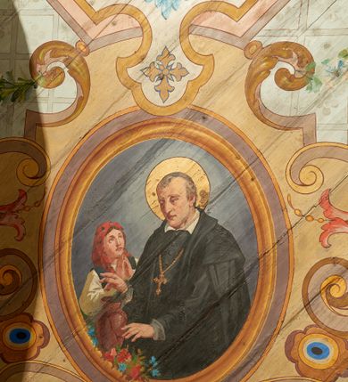 Zdjęcie nr 11: W prezbiterium w dolnej połowie ścian polichromia w formie namalowanej jasnoczerwonej, wielkowzorzytej tkaniny o motywach geometrycznych i roślinnych z niebieskim monogramem Marii i żółtymi koronami; jej górny brzeg odwiedziony jest pasem z brązowo-czerwoną dekoracją roślinną. Ściana przedzielona w połowie wysokości pasem z arkadkami wypełnionymi żółtymi wazonami oraz dekoracją roślinną na zielonym tle. W ich przyłuczach czerwone pola wypełnione malowaną roślinnością. W górnej połowie ścian malowane płyciny o jasnobrązowych ramach, których pola wypełnione są wzorem o motywie żółtych sześcioboków z fioletowymi kwiatami. Na południowej ścianie prezbiterium okna obwiedzione malowanymi, mazerowanymi ramami. W górnej części ściany, pod belkowaniem fryz utworzony z uskrzydlonych główek anielskich ukazanych na niebieskim tle, pomiędzy którymi znajdują się czerwone kampanule, pod nim podwieszone kwiatowe girlandy. Ściany zakończone profilowanym gzymsem, pomalowanym w dwa pasy – czerwony i niebieski, dekorowane motywem liści. Ściany podzielone lizenami w kolorze fioletowym, zdobionymi motywami geometrycznymi, różnymi w dolnej i górnej połowie. Strop prezbiterium z namalowaną płyciną w formie stojącego prostokąta, zamkniętego u dołu trójbocznie, o wklęsłych sześciu narożach, w których namalowana jest dekoracja roślinna. Płycina ujęta brązowo-żółtą ramą zdobioną motywem roślinnym oraz niebieskim pasem, z abstrakcyjnym motywem na wklęśnięciach. Różowe pole wypełnione białą kratką z kwiatami. W jego centrum owalny medalion w malowanej, profilowanej ramie oraz niebieskiej opasce z wypustkami, na których zawieszonych jest wokół osiem kwiatowych girland oraz cztery fantazyjne motywy kwiatowe. W medalionie namalowana scena Koronacji Matki Bożej. W jego centrum siedząca na obłokach Maria, ukazana frontalnie, z prawą ręką złożoną na piersi, lewą wyciągniętą w bok. Twarz ma pociągłą, o migdałowatych oczach, prostym nosie i pełnych ustach, okoloną długimi, falowanymi, jasnymi włosami. Ubrana jest w białą tunikę i niebieski płaszcz zarzucony na ramiona i kolana. Po jej prawej siedzi Chrystus, zwrócony w trzech czwartych w lewo, pochylony, prawą ręką podtrzymuje nad jej głową koronę. Twarz ma podłużną, o okrągłych oczach, lekko garbatym nosie i pełnych ustach, okolona brązowymi włosami i brodą. Ubrany jest w białą tunikę i czerwony płaszcz, o jego lewe ramię oparty jest krzyż. Po lewej stronie Marii siedzi Bóg Ojciec, zwrócony w trzech czwartych w prawo, lewą ręką przytrzymuje przy boku kulę, prawą podtrzymuje koronę nad głową Marii. Bóg ukazany jako starzec, o wysokim czole, podłużnej twarzy, małych oczach, garbatym nosie i pełnych ustach. Włosy i brodę ma długie i siwe. Ubrany jest w fioletową tunikę i jasnobrązowy płaszcz. Nad postaciami unosi się gołębica Ducha Świętego w glorii promienistej. Scena ukazana na tle błękitnego nieba, wypełnionego obłokami, w dolnej części obrazu z ukazanymi uskrzydlonymi główkami anielskimi. 
Ściany nawy w jednej trzeciej wysokości obwiedzione są pasem z malowanymi czerwono-brązowymi płycinami o naprzemiennym układzie owali i rombów, wypełnionymi dekoracją geometryczną i motywami roślinnymi. Ponad nimi wzdłuż ściany malowany niebieski pas o kolorowej i fantazyjnej dekoracji. Ściany w dwóch trzecich wysokości pokryte jasnoróżową polichromią o wielobarwnym, fantazyjnym, geometryczno-roślinnym wzorze z motywem równoramiennych krzyży. Ściany zakończone niebieskim fryzem przypominającym lambrekin z motywami geometrycznymi. Całość opasana profilowanym gzymsem, pomalowanym w dwa pasy – czerwony i niebieski, z dekoracją o motywach liści. Ściany podzielone lizenami pomalowanymi na kolor fioletowy, z dekoracją geometryczną. Na ścianach północnej i południowej po dwa okna obwiedzione malowanymi, mazerowanymi ramami. Pomiędzy oknami sceny w formie stojącego prostokąta zamkniętego łukiem półkolistym, w malowanej ramie dekorowanej cekinami. U dołu ramy fragment gzymsu dekorowanego kimationem z podwieszeniem zdobionym uskrzydloną główką anielską i meandrem. Rama zamknięta gzymsem wyłamanym na kształt łuku odcinkowego, podtrzymywanym na konsolach, dekorowanych motywem roślinnym. 
Na ścianie północnej scena z przedstawieniem św. Jakuba Większego z aniołem. W dolnej części obrazu święty w pozycji półleżącej, oparty o schody, ukazany frontalnie, z uniesioną głową, skierowaną w lewo i skrzyżowanymi na piersi rekami. Twarz ma owalną, o dużych oczach skierowanych w górę, prostym nosie i rozchylonych ustach, okoloną, krótkimi, jasnobrązowymi włosami i brodą. Wokół jego głowy nimb. Ubrany jest w ciemnobrązową tunikę, przepasaną sznurem, na lewym ramieniu ma muszlę, lewą ręką przytrzymuje laskę z bukłakiem. Na stopach ma sandały. Nad świętym unosi się anioł, zwrócony w trzech czwartych w lewo, w wykroku, z pochyloną głową, w prawej ręce trzyma liść palmy, w lewej, nad głową świętego - wieniec z róż. Anioł o młodzieńczej twarzy, z dużymi oczami zwróconymi w dół, dużym nosem i małymi ustami, okolonej jasnymi włosami sięgającymi ramion. Ubrany jest w żółtą tunikę oraz jasnofioletowy płaszcz. Ma białe i rozłożone skrzydła. Ukazany jest w otoczeniu obłoków. Poniżej, obok świętego na ziemi leży puklerz i miecz. Postacie ukazane we wnętrzu, z widoczną murowaną ścianą z oknami, fragmentem kolumny i schodami. W prawym dolnym sygnatura „M. Szczurowsk[i]”. 
Na ścianie południowej scena z przedstawieniem św. Izydora Oracza modlącego się przed kapliczką. W dolnej części obrazu święty w pozycji klęczącej, zwrócony profilem w prawo, z uniesionymi rękami o splecionych dłoniach w geście modlitwy, z uniesioną głową. Twarz ma szczupłą, o oczach skierowanych w górę, małym nosie i pełnych ustach, okoloną krótkimi, brązowymi włosami. Ubrany jest w białą koszulę, niebieski kaftan z czerwoną podszewką, przepasany w talii, z zawieszonym kluczem, na stopach ma buty. Przed nim, na ziemi leżą słomkowy kapelusz i bat. Przed świętym kapliczka w formie kamiennego krucyfiksu na cokole, pośród krzaków z kwiatami. Święty ukazany na tle pejzażu, z widocznym w oddali polem, na którym dwa woły ciągną pług, prowadzony przez anioła. Powyżej błękitne niebo zasnute ciemnymi chmurami, spod których wydobywa się strumień światła. W prawym dolnym rogu sygnatura „M. Szczurowski”. 
W zachodniej części nawy beżowa balustrada chóru muzycznego, na której namalowane są prostokątne płyciny, o krótszych bokach dekorowanych motywem roślinnym. Ich pola wypełnia niebieska opaska oraz różowa kratka ze zdobieniem roślinnym. Płycina środkowa w formie owalu z przedstawieniem Dawida, siedzącego na tronie i grającego na harfie. Postać ukazana do połowy, zwrócona w trzech czwartych w prawo, dwiema wyciągniętymi rękami dotyka strun harfy. Dawid o pociągłej twarzy, ze schematycznie oddanymi rysami, okolony brązowymi włosami i brodą. Na głowie ma koronę otwartą. Ubrany jest w czerwoną suknię, na ramiona ma narzuconą gronostajową pelerynę. Nad nim zawieszony czerwony baldachim, z zieloną podszewką. W oddali widoczny zarys zabudowań miejskich. Profile cokołu i gzymsu balustrady malowane w kolorowe pasy, z dekoracją roślinną. 
Na stropie nawy malowana płycina w formie stojącego prostokąta o zaokrąglonych narożach, ujęta niebieską ramą o geometrycznym wzorze, w miejscu naroży stylizowane roślinne palmety. W narożach płyciny cztery owalne medaliony z popiersiami św. Stanisława Kostki, św. Kazimierza Jagiellończyka, św. Stanisława z Piotrowinem i św. Jana Kantego. Medaliony ujęte są wolutowymi kartuszami, dekorowanymi stylizowanym ornamentem roślinnym. W polu centralnym malowanej płyciny scena ze św. Klemensem w formie stojącego prostokąta o wklęsłych narożach, ujęta malowaną ramą, w narożach uskrzydlone główki anielskie. Scena otoczona drugą ramą o fantazyjnym zarysie, dekorowaną na bokach fantazyjnymi szczytami z ornamentem roślinnym, które połączone są kwiecistymi girlandami z narożnymi kartuszami. Scena ze św. Klemensem przedstawia go w kamieniołomie, błogosławiącego robotników z kilofami. Święty ukazany jest jako starzec, z siwą brodą i włosami oraz łysiną na głowie. Ubrany jest w jasnofioletową sutannę, białą rokietę z dekoracyjnym obszyciem oraz jasnoczerwony, szeroki ornat, na piersi ma paliusz. W tle pomiędzy dwoma wzniesieniami skalnymi widoczne morze, z płynącym statkiem, w oddali zaś brzeg z domem. Na skarpie w lewej części obrazu ukazany baranek w glorii promienistej, na przeciwległej dwaj żołnierze, którzy zrzucili świętego z kotwicą zawieszoną u szyi do morza. Przy dolnej krawędzi obrazu sygnatura „pinxit 1910 / M. Szczurowski”.
