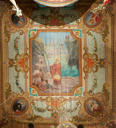 Zdjęcie nr 4: W prezbiterium w dolnej połowie ścian polichromia w formie namalowanej jasnoczerwonej, wielkowzorzytej tkaniny o motywach geometrycznych i roślinnych z niebieskim monogramem Marii i żółtymi koronami; jej górny brzeg odwiedziony jest pasem z brązowo-czerwoną dekoracją roślinną. Ściana przedzielona w połowie wysokości pasem z arkadkami wypełnionymi żółtymi wazonami oraz dekoracją roślinną na zielonym tle. W ich przyłuczach czerwone pola wypełnione malowaną roślinnością. W górnej połowie ścian malowane płyciny o jasnobrązowych ramach, których pola wypełnione są wzorem o motywie żółtych sześcioboków z fioletowymi kwiatami. Na południowej ścianie prezbiterium okna obwiedzione malowanymi, mazerowanymi ramami. W górnej części ściany, pod belkowaniem fryz utworzony z uskrzydlonych główek anielskich ukazanych na niebieskim tle, pomiędzy którymi znajdują się czerwone kampanule, pod nim podwieszone kwiatowe girlandy. Ściany zakończone profilowanym gzymsem, pomalowanym w dwa pasy – czerwony i niebieski, dekorowane motywem liści. Ściany podzielone lizenami w kolorze fioletowym, zdobionymi motywami geometrycznymi, różnymi w dolnej i górnej połowie. Strop prezbiterium z namalowaną płyciną w formie stojącego prostokąta, zamkniętego u dołu trójbocznie, o wklęsłych sześciu narożach, w których namalowana jest dekoracja roślinna. Płycina ujęta brązowo-żółtą ramą zdobioną motywem roślinnym oraz niebieskim pasem, z abstrakcyjnym motywem na wklęśnięciach. Różowe pole wypełnione białą kratką z kwiatami. W jego centrum owalny medalion w malowanej, profilowanej ramie oraz niebieskiej opasce z wypustkami, na których zawieszonych jest wokół osiem kwiatowych girland oraz cztery fantazyjne motywy kwiatowe. W medalionie namalowana scena Koronacji Matki Bożej. W jego centrum siedząca na obłokach Maria, ukazana frontalnie, z prawą ręką złożoną na piersi, lewą wyciągniętą w bok. Twarz ma pociągłą, o migdałowatych oczach, prostym nosie i pełnych ustach, okoloną długimi, falowanymi, jasnymi włosami. Ubrana jest w białą tunikę i niebieski płaszcz zarzucony na ramiona i kolana. Po jej prawej siedzi Chrystus, zwrócony w trzech czwartych w lewo, pochylony, prawą ręką podtrzymuje nad jej głową koronę. Twarz ma podłużną, o okrągłych oczach, lekko garbatym nosie i pełnych ustach, okolona brązowymi włosami i brodą. Ubrany jest w białą tunikę i czerwony płaszcz, o jego lewe ramię oparty jest krzyż. Po lewej stronie Marii siedzi Bóg Ojciec, zwrócony w trzech czwartych w prawo, lewą ręką przytrzymuje przy boku kulę, prawą podtrzymuje koronę nad głową Marii. Bóg ukazany jako starzec, o wysokim czole, podłużnej twarzy, małych oczach, garbatym nosie i pełnych ustach. Włosy i brodę ma długie i siwe. Ubrany jest w fioletową tunikę i jasnobrązowy płaszcz. Nad postaciami unosi się gołębica Ducha Świętego w glorii promienistej. Scena ukazana na tle błękitnego nieba, wypełnionego obłokami, w dolnej części obrazu z ukazanymi uskrzydlonymi główkami anielskimi. 
Ściany nawy w jednej trzeciej wysokości obwiedzione są pasem z malowanymi czerwono-brązowymi płycinami o naprzemiennym układzie owali i rombów, wypełnionymi dekoracją geometryczną i motywami roślinnymi. Ponad nimi wzdłuż ściany malowany niebieski pas o kolorowej i fantazyjnej dekoracji. Ściany w dwóch trzecich wysokości pokryte jasnoróżową polichromią o wielobarwnym, fantazyjnym, geometryczno-roślinnym wzorze z motywem równoramiennych krzyży. Ściany zakończone niebieskim fryzem przypominającym lambrekin z motywami geometrycznymi. Całość opasana profilowanym gzymsem, pomalowanym w dwa pasy – czerwony i niebieski, z dekoracją o motywach liści. Ściany podzielone lizenami pomalowanymi na kolor fioletowy, z dekoracją geometryczną. Na ścianach północnej i południowej po dwa okna obwiedzione malowanymi, mazerowanymi ramami. Pomiędzy oknami sceny w formie stojącego prostokąta zamkniętego łukiem półkolistym, w malowanej ramie dekorowanej cekinami. U dołu ramy fragment gzymsu dekorowanego kimationem z podwieszeniem zdobionym uskrzydloną główką anielską i meandrem. Rama zamknięta gzymsem wyłamanym na kształt łuku odcinkowego, podtrzymywanym na konsolach, dekorowanych motywem roślinnym. 
Na ścianie północnej scena z przedstawieniem św. Jakuba Większego z aniołem. W dolnej części obrazu święty w pozycji półleżącej, oparty o schody, ukazany frontalnie, z uniesioną głową, skierowaną w lewo i skrzyżowanymi na piersi rekami. Twarz ma owalną, o dużych oczach skierowanych w górę, prostym nosie i rozchylonych ustach, okoloną, krótkimi, jasnobrązowymi włosami i brodą. Wokół jego głowy nimb. Ubrany jest w ciemnobrązową tunikę, przepasaną sznurem, na lewym ramieniu ma muszlę, lewą ręką przytrzymuje laskę z bukłakiem. Na stopach ma sandały. Nad świętym unosi się anioł, zwrócony w trzech czwartych w lewo, w wykroku, z pochyloną głową, w prawej ręce trzyma liść palmy, w lewej, nad głową świętego - wieniec z róż. Anioł o młodzieńczej twarzy, z dużymi oczami zwróconymi w dół, dużym nosem i małymi ustami, okolonej jasnymi włosami sięgającymi ramion. Ubrany jest w żółtą tunikę oraz jasnofioletowy płaszcz. Ma białe i rozłożone skrzydła. Ukazany jest w otoczeniu obłoków. Poniżej, obok świętego na ziemi leży puklerz i miecz. Postacie ukazane we wnętrzu, z widoczną murowaną ścianą z oknami, fragmentem kolumny i schodami. W prawym dolnym sygnatura „M. Szczurowsk[i]”. 
Na ścianie południowej scena z przedstawieniem św. Izydora Oracza modlącego się przed kapliczką. W dolnej części obrazu święty w pozycji klęczącej, zwrócony profilem w prawo, z uniesionymi rękami o splecionych dłoniach w geście modlitwy, z uniesioną głową. Twarz ma szczupłą, o oczach skierowanych w górę, małym nosie i pełnych ustach, okoloną krótkimi, brązowymi włosami. Ubrany jest w białą koszulę, niebieski kaftan z czerwoną podszewką, przepasany w talii, z zawieszonym kluczem, na stopach ma buty. Przed nim, na ziemi leżą słomkowy kapelusz i bat. Przed świętym kapliczka w formie kamiennego krucyfiksu na cokole, pośród krzaków z kwiatami. Święty ukazany na tle pejzażu, z widocznym w oddali polem, na którym dwa woły ciągną pług, prowadzony przez anioła. Powyżej błękitne niebo zasnute ciemnymi chmurami, spod których wydobywa się strumień światła. W prawym dolnym rogu sygnatura „M. Szczurowski”. 
W zachodniej części nawy beżowa balustrada chóru muzycznego, na której namalowane są prostokątne płyciny, o krótszych bokach dekorowanych motywem roślinnym. Ich pola wypełnia niebieska opaska oraz różowa kratka ze zdobieniem roślinnym. Płycina środkowa w formie owalu z przedstawieniem Dawida, siedzącego na tronie i grającego na harfie. Postać ukazana do połowy, zwrócona w trzech czwartych w prawo, dwiema wyciągniętymi rękami dotyka strun harfy. Dawid o pociągłej twarzy, ze schematycznie oddanymi rysami, okolony brązowymi włosami i brodą. Na głowie ma koronę otwartą. Ubrany jest w czerwoną suknię, na ramiona ma narzuconą gronostajową pelerynę. Nad nim zawieszony czerwony baldachim, z zieloną podszewką. W oddali widoczny zarys zabudowań miejskich. Profile cokołu i gzymsu balustrady malowane w kolorowe pasy, z dekoracją roślinną. 
Na stropie nawy malowana płycina w formie stojącego prostokąta o zaokrąglonych narożach, ujęta niebieską ramą o geometrycznym wzorze, w miejscu naroży stylizowane roślinne palmety. W narożach płyciny cztery owalne medaliony z popiersiami św. Stanisława Kostki, św. Kazimierza Jagiellończyka, św. Stanisława z Piotrowinem i św. Jana Kantego. Medaliony ujęte są wolutowymi kartuszami, dekorowanymi stylizowanym ornamentem roślinnym. W polu centralnym malowanej płyciny scena ze św. Klemensem w formie stojącego prostokąta o wklęsłych narożach, ujęta malowaną ramą, w narożach uskrzydlone główki anielskie. Scena otoczona drugą ramą o fantazyjnym zarysie, dekorowaną na bokach fantazyjnymi szczytami z ornamentem roślinnym, które połączone są kwiecistymi girlandami z narożnymi kartuszami. Scena ze św. Klemensem przedstawia go w kamieniołomie, błogosławiącego robotników z kilofami. Święty ukazany jest jako starzec, z siwą brodą i włosami oraz łysiną na głowie. Ubrany jest w jasnofioletową sutannę, białą rokietę z dekoracyjnym obszyciem oraz jasnoczerwony, szeroki ornat, na piersi ma paliusz. W tle pomiędzy dwoma wzniesieniami skalnymi widoczne morze, z płynącym statkiem, w oddali zaś brzeg z domem. Na skarpie w lewej części obrazu ukazany baranek w glorii promienistej, na przeciwległej dwaj żołnierze, którzy zrzucili świętego z kotwicą zawieszoną u szyi do morza. Przy dolnej krawędzi obrazu sygnatura „pinxit 1910 / M. Szczurowski”.
