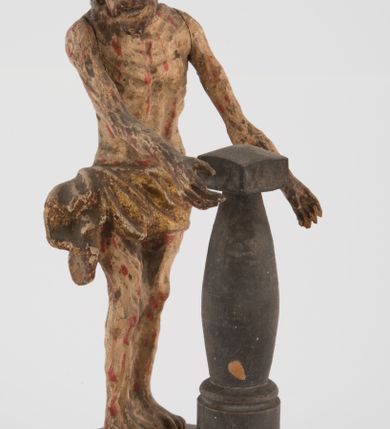 Zdjęcie nr 4: Pełnoplastyczna figurka Chrystusa z ruchomymi rękami, stojącego przy słupie ustawiona jest na owalnej podstawie. Chrystus stoi w wykroku, delikatnie pochylony ku słupowi, z głową skierowaną w prawo, z rękami wysuniętymi przed siebie, ujmującymi słup biczowania. Twarz ma szczupłą, pociągłą, o uwypuklonych kościach policzkowych, dużych oczach i nosie, okoloną krótką brodą i długimi, falowanymi włosami opadającymi na plecy. Ciało Chrystusa jest wychudzone, z silnie uwypuklonymi żebrami klatki piersiowej. Przez biodra ma przewiązane krótkie, obficie drapowane, złocone perizonium ze zwisem tkaniny na prawym boku. Słup w formie tralki na cokole. Polichromia ciała naturalistyczna, z zaznaczonymi licznymi strużkami krwi. 
