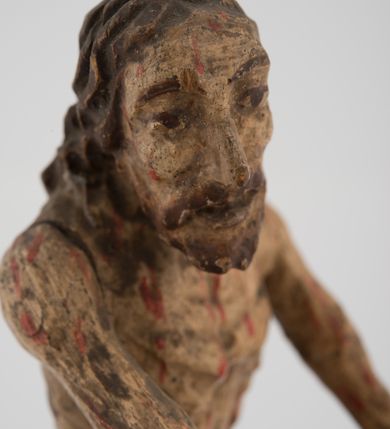 Zdjęcie nr 3: Pełnoplastyczna figurka Chrystusa z ruchomymi rękami, stojącego przy słupie ustawiona jest na owalnej podstawie. Chrystus stoi w wykroku, delikatnie pochylony ku słupowi, z głową skierowaną w prawo, z rękami wysuniętymi przed siebie, ujmującymi słup biczowania. Twarz ma szczupłą, pociągłą, o uwypuklonych kościach policzkowych, dużych oczach i nosie, okoloną krótką brodą i długimi, falowanymi włosami opadającymi na plecy. Ciało Chrystusa jest wychudzone, z silnie uwypuklonymi żebrami klatki piersiowej. Przez biodra ma przewiązane krótkie, obficie drapowane, złocone perizonium ze zwisem tkaniny na prawym boku. Słup w formie tralki na cokole. Polichromia ciała naturalistyczna, z zaznaczonymi licznymi strużkami krwi. 
