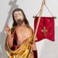 Zdjęcie nr 1: Figura pełnoplastyczna, ustawiona na rzeźbionym fragmencie podłoża i na niskiej podstawie na planie ośmioboku. Chrystus zwrócony jest frontalnie, z głową skierowaną w prawo. W lewej ręce trzyma drzewce zakończone krzyżem z chorągwią z tkaniny z naszytym krzyżem, prawą rękę unosi w geście błogosławieństwa. Twarz ma owalną, o dużych, półprzymkniętych oczach, uniesionych brwiach, dużym nosie i małych ustach, okoloną krótką brodą skręconą w dwa pukle oraz brązowymi włosami sięgającymi ramion, rzeźbionymi w regularne fale. Chrystus ubrany jest w złocony płaszcz z czerwoną podszewką zarzucony na ramiona i plecy, otaczający postać i zarzucony z przodu na lewe przedramię, odsłaniając nagi tors z zaznaczoną raną w boku. Polichromia ciała naturalistyczna.
