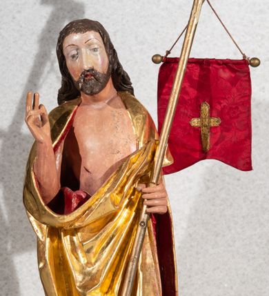 Zdjęcie nr 1: Figura pełnoplastyczna, ustawiona na rzeźbionym fragmencie podłoża i na niskiej podstawie na planie ośmioboku. Chrystus zwrócony jest frontalnie, z głową skierowaną w prawo. W lewej ręce trzyma drzewce zakończone krzyżem z chorągwią z tkaniny z naszytym krzyżem, prawą rękę unosi w geście błogosławieństwa. Twarz ma owalną, o dużych, półprzymkniętych oczach, uniesionych brwiach, dużym nosie i małych ustach, okoloną krótką brodą skręconą w dwa pukle oraz brązowymi włosami sięgającymi ramion, rzeźbionymi w regularne fale. Chrystus ubrany jest w złocony płaszcz z czerwoną podszewką zarzucony na ramiona i plecy, otaczający postać i zarzucony z przodu na lewe przedramię, odsłaniając nagi tors z zaznaczoną raną w boku. Polichromia ciała naturalistyczna.
