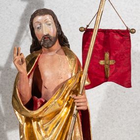 Zdjęcie nr 1: Figura pełnoplastyczna, ustawiona na rzeźbionym fragmencie podłoża i na niskiej podstawie na planie ośmioboku. Chrystus zwrócony jest frontalnie, z głową skierowaną w prawo. W lewej ręce trzyma drzewce zakończone krzyżem z chorągwią z tkaniny z naszytym krzyżem, prawą rękę unosi w geście błogosławieństwa. Twarz ma owalną, o dużych, półprzymkniętych oczach, uniesionych brwiach, dużym nosie i małych ustach, okoloną krótką brodą skręconą w dwa pukle oraz brązowymi włosami sięgającymi ramion, rzeźbionymi w regularne fale. Chrystus ubrany jest w złocony płaszcz z czerwoną podszewką zarzucony na ramiona i plecy, otaczający postać i zarzucony z przodu na lewe przedramię, odsłaniając nagi tors z zaznaczoną raną w boku. Polichromia ciała naturalistyczna.
