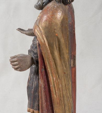 Zdjęcie nr 6: Rzeźba pełnoplastyczna, nieopracowana z tyłu, ustawiona na podstawie o nieregularnym kształcie. Święty zwrócony jest frontalnie, w delikatnym kontrapoście, z obiema rękami ugiętymi i wyciągniętymi do przodu. Prawa dłoń wysunięta zwrócona ku górze, w lewej trzyma laskę zakończoną krzyżem na kuli. Twarz ma kwadratową, o dużych oczach, krótkim nosie i małych, pełnych ustach, okoloną gęstą siwą brodą oraz falowanymi włosami, sięgającymi ramion. Mikołaj ubrany jest w długą, zieloną albę, niebieską rokietę zdobioną u dołu oraz zarzucony na ramiona, spięty na piersiach klamrą, pozłacany płaszcz, na głowie ma złoconą infułę. Polichromia ciała naturalistyczna, o jasnej, lekko zaróżowionej karnacji.
