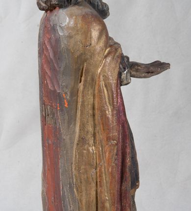 Zdjęcie nr 7: Rzeźba pełnoplastyczna, nieopracowana z tyłu, ustawiona na podstawie o nieregularnym kształcie. Święty zwrócony jest frontalnie, w delikatnym kontrapoście, z obiema rękami ugiętymi i wyciągniętymi do przodu. Prawa dłoń wysunięta zwrócona ku górze, w lewej trzyma laskę zakończoną krzyżem na kuli. Twarz ma kwadratową, o dużych oczach, krótkim nosie i małych, pełnych ustach, okoloną gęstą siwą brodą oraz falowanymi włosami, sięgającymi ramion. Mikołaj ubrany jest w długą, zieloną albę, niebieską rokietę zdobioną u dołu oraz zarzucony na ramiona, spięty na piersiach klamrą, pozłacany płaszcz, na głowie ma złoconą infułę. Polichromia ciała naturalistyczna, o jasnej, lekko zaróżowionej karnacji.
