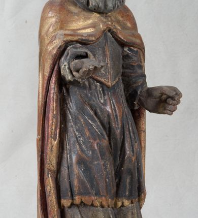 Zdjęcie nr 8: Rzeźba pełnoplastyczna, nieopracowana z tyłu, ustawiona na podstawie o nieregularnym kształcie. Święty zwrócony jest frontalnie, w delikatnym kontrapoście, z obiema rękami ugiętymi i wyciągniętymi do przodu. Prawa dłoń wysunięta zwrócona ku górze, w lewej trzyma laskę zakończoną krzyżem na kuli. Twarz ma kwadratową, o dużych oczach, krótkim nosie i małych, pełnych ustach, okoloną gęstą siwą brodą oraz falowanymi włosami, sięgającymi ramion. Mikołaj ubrany jest w długą, zieloną albę, niebieską rokietę zdobioną u dołu oraz zarzucony na ramiona, spięty na piersiach klamrą, pozłacany płaszcz, na głowie ma złoconą infułę. Polichromia ciała naturalistyczna, o jasnej, lekko zaróżowionej karnacji.
