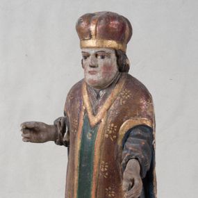 Zdjęcie nr 1: Rzeźba pełnoplastyczna, nieopracowana z tyłu, ustawiona jest na zielonej podstawie o nieregularnym kształcie. Święty zwrócony jest frontalnie, z obiema rękami ugiętymi, wyciągniętymi do przodu. Ma kwadratową twarz, o podkreślonej linii żuchwy i brody, o dużych oczach, krótkim nosie i małych, pełnych ustach. Włosy ma brązowe, falowane sięgające ramion. Ubrany jest w szarą, silnie drapowaną u dołu albę, widoczny u szyi humerał oraz złocony ornat skrzypcowy o wzorze kwiatowym, z pretekstą przednią w kolorze zielonym i niebieską podszewką. Na głowie ma złoconą mitrę. Polichromia ciała naturalistyczna o jasnej, zaróżowionej karnacji w partii twarzy.