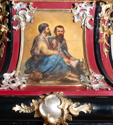 Zdjęcie nr 5: Ambona przyścienna, wisząca z dostępem od zakrystii. Podwieszenie w formie odwróconego ostrosłupa o ściętym wierzchołku, na krawędziach flankowane pilastrami zakończonymi u góry wolutowo, a na ściankach zdobione płycinami. Kosz na planie kwadratu umieszczony na wybrzuszonej podstawie, dekorowanej rocaille'owymi kartuszami, o ściętych górnych narożach; ścianki wklęsłe, zwężające się ku górze, ujęte w narożach pilastrami z trzonami dekorowanymi rocaille'em i zwisami z różanych gałązek. Podpory dźwigają gzyms wyłamany na ich osi, tworzący parapet. W polu ścianek płyciny z rocaille'ami w narożach z malowanymi olejem na desce obrazami przedstawiającymi ewangelistów. Od strony lewej: św. Mateusz z aniołem, pośrodku św. Marek z lwem i św. Łukasz z wołem, a po prawej św. Jan z orłem. Ewangeliści ukazani w pozycji siedzącej z księgami w dłoniach, ubrani w różnokolorowe, powłóczyste szaty na złotym tle. Zaplecek w kształcie stojącego prostokąta, ujęty pilastrami dekorowanymi rocaille'ami. W polu płycina w kształcie stojącego prostokąta, zamkniętego łukiem nadwieszonym z płaskorzeźbionymi tablicami dekalogu, ujętymi od dołu skrzyżowanymi gałązkami oliwnymi, związanymi wstęgą. Belkowanie nad zapleckiem o wypukłej linii, z przerwanym pośrodku gzymsem, od góry wypełnionym rocaille'em, od dołu ozdobionym podwieszonym lambrekinem z chwostami. Zwieńczenie ma formę zbliżoną do trapezu, ujęte jest wolutami spływającymi na belkowanie, na których ustawione są rokokowe wazony. W polu zwieńczenia znajduje się medalion z glorią pośród obłoków, a powyżej gołębica Ducha Świętego. Zwieńczenie flankują umocowane na ścianie, uskrzydlone główki aniołków dobrej i złej rady: po lewej o jasnej karnacji, a po prawej o czarnej karnacji. Szczyt zwieńczenia ma formę gzymsu z podwieszonym lambrekinem. Całość wieńczy zawieszona na ścianie promienista gloria z wieńcem utworzonym z obłoków. Struktura polichromowana jest w kolorze czerwonym, z czarnymi profilami oraz złoconą i srebrzoną ornamentyką. 
