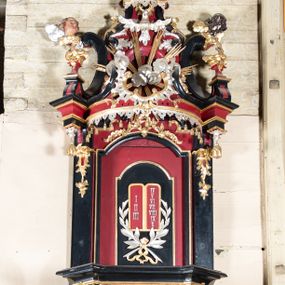 Zdjęcie nr 1: Ambona przyścienna, wisząca z dostępem od zakrystii. Podwieszenie w formie odwróconego ostrosłupa o ściętym wierzchołku, na krawędziach flankowane pilastrami zakończonymi u góry wolutowo, a na ściankach zdobione płycinami. Kosz na planie kwadratu umieszczony na wybrzuszonej podstawie, dekorowanej rocaille'owymi kartuszami, o ściętych górnych narożach; ścianki wklęsłe, zwężające się ku górze, ujęte w narożach pilastrami z trzonami dekorowanymi rocaille'em i zwisami z różanych gałązek. Podpory dźwigają gzyms wyłamany na ich osi, tworzący parapet. W polu ścianek płyciny z rocaille'ami w narożach z malowanymi olejem na desce obrazami przedstawiającymi ewangelistów. Od strony lewej: św. Mateusz z aniołem, pośrodku św. Marek z lwem i św. Łukasz z wołem, a po prawej św. Jan z orłem. Ewangeliści ukazani w pozycji siedzącej z księgami w dłoniach, ubrani w różnokolorowe, powłóczyste szaty na złotym tle. Zaplecek w kształcie stojącego prostokąta, ujęty pilastrami dekorowanymi rocaille'ami. W polu płycina w kształcie stojącego prostokąta, zamkniętego łukiem nadwieszonym z płaskorzeźbionymi tablicami dekalogu, ujętymi od dołu skrzyżowanymi gałązkami oliwnymi, związanymi wstęgą. Belkowanie nad zapleckiem o wypukłej linii, z przerwanym pośrodku gzymsem, od góry wypełnionym rocaille'em, od dołu ozdobionym podwieszonym lambrekinem z chwostami. Zwieńczenie ma formę zbliżoną do trapezu, ujęte jest wolutami spływającymi na belkowanie, na których ustawione są rokokowe wazony. W polu zwieńczenia znajduje się medalion z glorią pośród obłoków, a powyżej gołębica Ducha Świętego. Zwieńczenie flankują umocowane na ścianie, uskrzydlone główki aniołków dobrej i złej rady: po lewej o jasnej karnacji, a po prawej o czarnej karnacji. Szczyt zwieńczenia ma formę gzymsu z podwieszonym lambrekinem. Całość wieńczy zawieszona na ścianie promienista gloria z wieńcem utworzonym z obłoków. Struktura polichromowana jest w kolorze czerwonym, z czarnymi profilami oraz złoconą i srebrzoną ornamentyką. 
