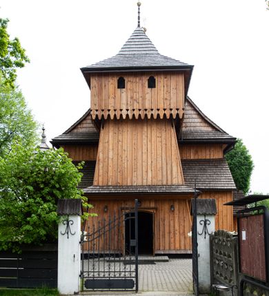 Zdjęcie nr 2: Kościół orientowany, drewniany o konstrukcji zrębowej z wieżą o konstrukcji słupowo-ryglowej na rzucie kwadratu. Nawa prostokątna z węższym, prostokątnym prezbiterium zamkniętym trójboczną absydą. Przy prezbiterium, od północy znajduje się zakrystia, a przy nawie, od południa – kruchta. Na osi nawy, od zachodu wieża o pochyłych ścianach z nadwieszoną izbicą. W kościele sześć otworów okiennych w kształcie stojących prostokątów, ujętych opaskami z prostych listew: dwa od strony północnej i cztery od strony południowej. Na zewnątrz okien zamontowane są współczesne kraty z ozdobnych prętów. Główne wejście do kościoła od zachodu w przyziemiu wieży. Dach dwuspadowy, od wschodu trójspadowy, wykonany w konstrukcji krokwiowo-jętkowej z podwójnymi jętkami, kryty gontem. Zakrystia zadaszona przedłużoną połacią głównego dachu. Na osi kalenicy dachu wieżyczka na sygnaturkę, barokowa z latarnią, kryta blachą miedzianą. Z zewnątrz ściany kościoła i wieży pokryto szalunkiem pionowym z listwami na stykach łączenia desek. Nadwieszona izbica wieży z wyciętymi ornamentami na dolnych zakończeniach desek. W czterech ścianach izbicy po dwa okna w kształcie stojącego prostokąta, zamknięte łukiem nadwieszonym. Wieża nakryta daszkiem czterospadowym, krytym gontem. Do obu stron wieży dostawione nowe dobudówki: w południowej umieszczono schody na chór muzyczny, a w północnej znajdują się pomieszczenia gospodarcze. Kościół w przyziemiu jest podbudowany betonowym cokołem, silnie wysuniętym przed lico ścian i zabezpieczony małym daszkiem.

