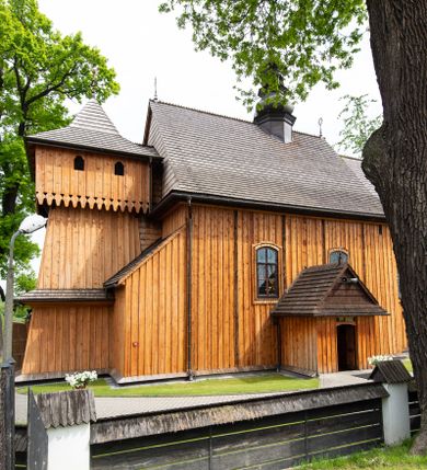Zdjęcie nr 1: Kościół orientowany, drewniany o konstrukcji zrębowej z wieżą o konstrukcji słupowo-ryglowej na rzucie kwadratu. Nawa prostokątna z węższym, prostokątnym prezbiterium zamkniętym trójboczną absydą. Przy prezbiterium, od północy znajduje się zakrystia, a przy nawie, od południa – kruchta. Na osi nawy, od zachodu wieża o pochyłych ścianach z nadwieszoną izbicą. W kościele sześć otworów okiennych w kształcie stojących prostokątów, ujętych opaskami z prostych listew: dwa od strony północnej i cztery od strony południowej. Na zewnątrz okien zamontowane są współczesne kraty z ozdobnych prętów. Główne wejście do kościoła od zachodu w przyziemiu wieży. Dach dwuspadowy, od wschodu trójspadowy, wykonany w konstrukcji krokwiowo-jętkowej z podwójnymi jętkami, kryty gontem. Zakrystia zadaszona przedłużoną połacią głównego dachu. Na osi kalenicy dachu wieżyczka na sygnaturkę, barokowa z latarnią, kryta blachą miedzianą. Z zewnątrz ściany kościoła i wieży pokryto szalunkiem pionowym z listwami na stykach łączenia desek. Nadwieszona izbica wieży z wyciętymi ornamentami na dolnych zakończeniach desek. W czterech ścianach izbicy po dwa okna w kształcie stojącego prostokąta, zamknięte łukiem nadwieszonym. Wieża nakryta daszkiem czterospadowym, krytym gontem. Do obu stron wieży dostawione nowe dobudówki: w południowej umieszczono schody na chór muzyczny, a w północnej znajdują się pomieszczenia gospodarcze. Kościół w przyziemiu jest podbudowany betonowym cokołem, silnie wysuniętym przed lico ścian i zabezpieczony małym daszkiem.

