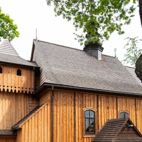 Zdjęcie nr 1: Kościół orientowany, drewniany o konstrukcji zrębowej z wieżą o konstrukcji słupowo-ryglowej na rzucie kwadratu. Nawa prostokątna z węższym, prostokątnym prezbiterium zamkniętym trójboczną absydą. Przy prezbiterium, od północy znajduje się zakrystia, a przy nawie, od południa – kruchta. Na osi nawy, od zachodu wieża o pochyłych ścianach z nadwieszoną izbicą. W kościele sześć otworów okiennych w kształcie stojących prostokątów, ujętych opaskami z prostych listew: dwa od strony północnej i cztery od strony południowej. Na zewnątrz okien zamontowane są współczesne kraty z ozdobnych prętów. Główne wejście do kościoła od zachodu w przyziemiu wieży. Dach dwuspadowy, od wschodu trójspadowy, wykonany w konstrukcji krokwiowo-jętkowej z podwójnymi jętkami, kryty gontem. Zakrystia zadaszona przedłużoną połacią głównego dachu. Na osi kalenicy dachu wieżyczka na sygnaturkę, barokowa z latarnią, kryta blachą miedzianą. Z zewnątrz ściany kościoła i wieży pokryto szalunkiem pionowym z listwami na stykach łączenia desek. Nadwieszona izbica wieży z wyciętymi ornamentami na dolnych zakończeniach desek. W czterech ścianach izbicy po dwa okna w kształcie stojącego prostokąta, zamknięte łukiem nadwieszonym. Wieża nakryta daszkiem czterospadowym, krytym gontem. Do obu stron wieży dostawione nowe dobudówki: w południowej umieszczono schody na chór muzyczny, a w północnej znajdują się pomieszczenia gospodarcze. Kościół w przyziemiu jest podbudowany betonowym cokołem, silnie wysuniętym przed lico ścian i zabezpieczony małym daszkiem.

