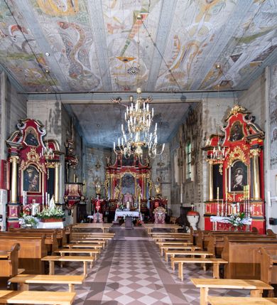 Zdjęcie nr 8: Kościół orientowany, drewniany o konstrukcji zrębowej z wieżą o konstrukcji słupowo-ryglowej na rzucie kwadratu. Nawa prostokątna z węższym, prostokątnym prezbiterium zamkniętym trójboczną absydą. Przy prezbiterium, od północy znajduje się zakrystia, a przy nawie, od południa – kruchta. Na osi nawy, od zachodu wieża o pochyłych ścianach z nadwieszoną izbicą. W kościele sześć otworów okiennych w kształcie stojących prostokątów, ujętych opaskami z prostych listew: dwa od strony północnej i cztery od strony południowej. Na zewnątrz okien zamontowane są współczesne kraty z ozdobnych prętów. Główne wejście do kościoła od zachodu w przyziemiu wieży. Dach dwuspadowy, od wschodu trójspadowy, wykonany w konstrukcji krokwiowo-jętkowej z podwójnymi jętkami, kryty gontem. Zakrystia zadaszona przedłużoną połacią głównego dachu. Na osi kalenicy dachu wieżyczka na sygnaturkę, barokowa z latarnią, kryta blachą miedzianą. Z zewnątrz ściany kościoła i wieży pokryto szalunkiem pionowym z listwami na stykach łączenia desek. Nadwieszona izbica wieży z wyciętymi ornamentami na dolnych zakończeniach desek. W czterech ścianach izbicy po dwa okna w kształcie stojącego prostokąta, zamknięte łukiem nadwieszonym. Wieża nakryta daszkiem czterospadowym, krytym gontem. Do obu stron wieży dostawione nowe dobudówki: w południowej umieszczono schody na chór muzyczny, a w północnej znajdują się pomieszczenia gospodarcze. Kościół w przyziemiu jest podbudowany betonowym cokołem, silnie wysuniętym przed lico ścian i zabezpieczony małym daszkiem.

