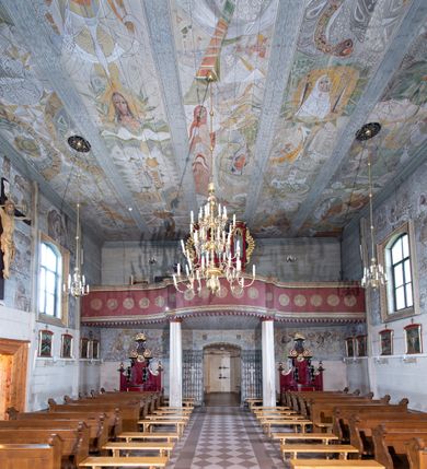 Zdjęcie nr 10: Kościół orientowany, drewniany o konstrukcji zrębowej z wieżą o konstrukcji słupowo-ryglowej na rzucie kwadratu. Nawa prostokątna z węższym, prostokątnym prezbiterium zamkniętym trójboczną absydą. Przy prezbiterium, od północy znajduje się zakrystia, a przy nawie, od południa – kruchta. Na osi nawy, od zachodu wieża o pochyłych ścianach z nadwieszoną izbicą. W kościele sześć otworów okiennych w kształcie stojących prostokątów, ujętych opaskami z prostych listew: dwa od strony północnej i cztery od strony południowej. Na zewnątrz okien zamontowane są współczesne kraty z ozdobnych prętów. Główne wejście do kościoła od zachodu w przyziemiu wieży. Dach dwuspadowy, od wschodu trójspadowy, wykonany w konstrukcji krokwiowo-jętkowej z podwójnymi jętkami, kryty gontem. Zakrystia zadaszona przedłużoną połacią głównego dachu. Na osi kalenicy dachu wieżyczka na sygnaturkę, barokowa z latarnią, kryta blachą miedzianą. Z zewnątrz ściany kościoła i wieży pokryto szalunkiem pionowym z listwami na stykach łączenia desek. Nadwieszona izbica wieży z wyciętymi ornamentami na dolnych zakończeniach desek. W czterech ścianach izbicy po dwa okna w kształcie stojącego prostokąta, zamknięte łukiem nadwieszonym. Wieża nakryta daszkiem czterospadowym, krytym gontem. Do obu stron wieży dostawione nowe dobudówki: w południowej umieszczono schody na chór muzyczny, a w północnej znajdują się pomieszczenia gospodarcze. Kościół w przyziemiu jest podbudowany betonowym cokołem, silnie wysuniętym przed lico ścian i zabezpieczony małym daszkiem.

