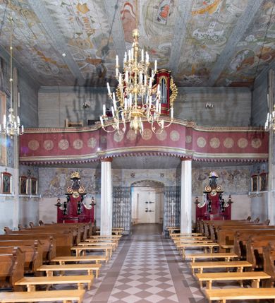 Zdjęcie nr 9: Kościół orientowany, drewniany o konstrukcji zrębowej z wieżą o konstrukcji słupowo-ryglowej na rzucie kwadratu. Nawa prostokątna z węższym, prostokątnym prezbiterium zamkniętym trójboczną absydą. Przy prezbiterium, od północy znajduje się zakrystia, a przy nawie, od południa – kruchta. Na osi nawy, od zachodu wieża o pochyłych ścianach z nadwieszoną izbicą. W kościele sześć otworów okiennych w kształcie stojących prostokątów, ujętych opaskami z prostych listew: dwa od strony północnej i cztery od strony południowej. Na zewnątrz okien zamontowane są współczesne kraty z ozdobnych prętów. Główne wejście do kościoła od zachodu w przyziemiu wieży. Dach dwuspadowy, od wschodu trójspadowy, wykonany w konstrukcji krokwiowo-jętkowej z podwójnymi jętkami, kryty gontem. Zakrystia zadaszona przedłużoną połacią głównego dachu. Na osi kalenicy dachu wieżyczka na sygnaturkę, barokowa z latarnią, kryta blachą miedzianą. Z zewnątrz ściany kościoła i wieży pokryto szalunkiem pionowym z listwami na stykach łączenia desek. Nadwieszona izbica wieży z wyciętymi ornamentami na dolnych zakończeniach desek. W czterech ścianach izbicy po dwa okna w kształcie stojącego prostokąta, zamknięte łukiem nadwieszonym. Wieża nakryta daszkiem czterospadowym, krytym gontem. Do obu stron wieży dostawione nowe dobudówki: w południowej umieszczono schody na chór muzyczny, a w północnej znajdują się pomieszczenia gospodarcze. Kościół w przyziemiu jest podbudowany betonowym cokołem, silnie wysuniętym przed lico ścian i zabezpieczony małym daszkiem.

