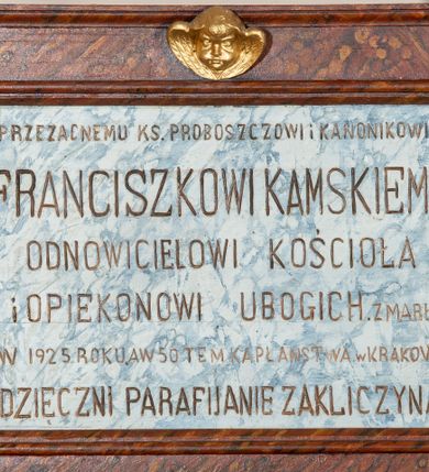 Zdjęcie nr 1: Epitafium w kształcie leżącego prostokąta z profilowanym obramieniem z uszakami. Na osi, w górnej części złocona, uskrzydlona główka aniołka, a w narożach złocone rozety. Pośrodku tablicy inskrypcja „PRZEZACNEMU KS(IĘDZU) PROBOSZCZOWI I KANONIKOWI / FRANCISZKOWI KAMSKIEMU / ODNOWICIELOWI KOŚCIOŁA / i OPIEKUNOWI UBOGICH. ZMARŁEMU / W 1925 ROKU. A W 50 TEM KAPŁAŃSTWA w KRAKOWIE / WDZIĘCZNI PARAFIJANIE ZAKLICZYNA.” Pole epitafium marmoryzowane w kolorze niebieskim, a rama marmoryzowana w kolorze ciemnobrązowym.