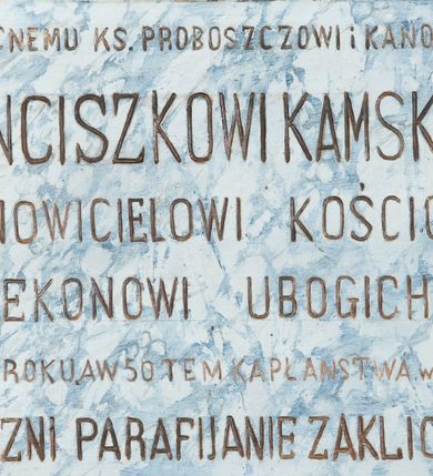 Zdjęcie nr 2: Epitafium w kształcie leżącego prostokąta z profilowanym obramieniem z uszakami. Na osi, w górnej części złocona, uskrzydlona główka aniołka, a w narożach złocone rozety. Pośrodku tablicy inskrypcja „PRZEZACNEMU KS(IĘDZU) PROBOSZCZOWI I KANONIKOWI / FRANCISZKOWI KAMSKIEMU / ODNOWICIELOWI KOŚCIOŁA / i OPIEKUNOWI UBOGICH. ZMARŁEMU / W 1925 ROKU. A W 50 TEM KAPŁAŃSTWA w KRAKOWIE / WDZIĘCZNI PARAFIJANIE ZAKLICZYNA.” Pole epitafium marmoryzowane w kolorze niebieskim, a rama marmoryzowana w kolorze ciemnobrązowym.