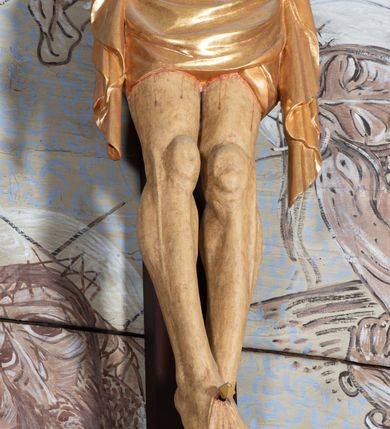 Zdjęcie nr 4: Figura Chrystusa przybita do krzyża trzema gwoździami pełna, niedrążona. Ciało w niewielkim zwisie, głowa delikatnie opada na prawy bark, stopy skrzyżowane w układzie prawa na lewą. Sylwetka podkreślona wydatną klatką piersiową, z wyraźnie zaznaczoną linią żeber i mostka, a także z precyzyjnie ukazaną anatomią. Twarz podłużna, z długim nosem, przymkniętymi oczami, okolona brodą ułożoną w długie, równolegle opadające, proste pukle. Włosy długie, brązowe, spływające na plecy oraz z przodu dwoma, silnie skręconymi lokami. Na głowie zielona korona cierniowa, a wokół niej nimb krzyżowy złożony z trzech wiązek promieni. Perizonium ciasno oplatające biodra, z dwoma zwisami po bokach, po lewej stronie dłuższym. Polichromia ciała naturalistyczna z delikatnie zaznaczonymi śladami męki, perizonium, gwoździe i nimb złocone. Nad głową Chrystusa titulus w formie pionowej banderoli z napisem „J[esus] N[azarenus] / R[ex] J[udaeorum]”.