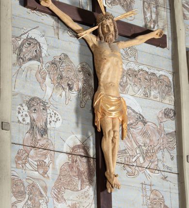 Zdjęcie nr 6: Figura Chrystusa przybita do krzyża trzema gwoździami pełna, niedrążona. Ciało w niewielkim zwisie, głowa delikatnie opada na prawy bark, stopy skrzyżowane w układzie prawa na lewą. Sylwetka podkreślona wydatną klatką piersiową, z wyraźnie zaznaczoną linią żeber i mostka, a także z precyzyjnie ukazaną anatomią. Twarz podłużna, z długim nosem, przymkniętymi oczami, okolona brodą ułożoną w długie, równolegle opadające, proste pukle. Włosy długie, brązowe, spływające na plecy oraz z przodu dwoma, silnie skręconymi lokami. Na głowie zielona korona cierniowa, a wokół niej nimb krzyżowy złożony z trzech wiązek promieni. Perizonium ciasno oplatające biodra, z dwoma zwisami po bokach, po lewej stronie dłuższym. Polichromia ciała naturalistyczna z delikatnie zaznaczonymi śladami męki, perizonium, gwoździe i nimb złocone. Nad głową Chrystusa titulus w formie pionowej banderoli z napisem „J[esus] N[azarenus] / R[ex] J[udaeorum]”.