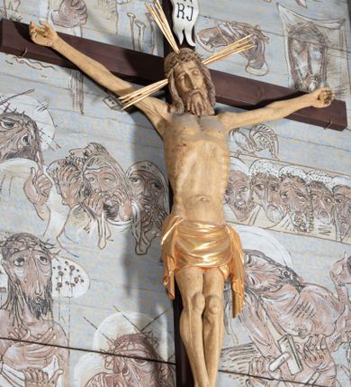 Zdjęcie nr 1: Figura Chrystusa przybita do krzyża trzema gwoździami pełna, niedrążona. Ciało w niewielkim zwisie, głowa delikatnie opada na prawy bark, stopy skrzyżowane w układzie prawa na lewą. Sylwetka podkreślona wydatną klatką piersiową, z wyraźnie zaznaczoną linią żeber i mostka, a także z precyzyjnie ukazaną anatomią. Twarz podłużna, z długim nosem, przymkniętymi oczami, okolona brodą ułożoną w długie, równolegle opadające, proste pukle. Włosy długie, brązowe, spływające na plecy oraz z przodu dwoma, silnie skręconymi lokami. Na głowie zielona korona cierniowa, a wokół niej nimb krzyżowy złożony z trzech wiązek promieni. Perizonium ciasno oplatające biodra, z dwoma zwisami po bokach, po lewej stronie dłuższym. Polichromia ciała naturalistyczna z delikatnie zaznaczonymi śladami męki, perizonium, gwoździe i nimb złocone. Nad głową Chrystusa titulus w formie pionowej banderoli z napisem „J[esus] N[azarenus] / R[ex] J[udaeorum]”.