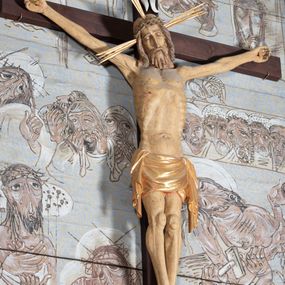 Zdjęcie nr 1: Figura Chrystusa przybita do krzyża trzema gwoździami pełna, niedrążona. Ciało w niewielkim zwisie, głowa delikatnie opada na prawy bark, stopy skrzyżowane w układzie prawa na lewą. Sylwetka podkreślona wydatną klatką piersiową, z wyraźnie zaznaczoną linią żeber i mostka, a także z precyzyjnie ukazaną anatomią. Twarz podłużna, z długim nosem, przymkniętymi oczami, okolona brodą ułożoną w długie, równolegle opadające, proste pukle. Włosy długie, brązowe, spływające na plecy oraz z przodu dwoma, silnie skręconymi lokami. Na głowie zielona korona cierniowa, a wokół niej nimb krzyżowy złożony z trzech wiązek promieni. Perizonium ciasno oplatające biodra, z dwoma zwisami po bokach, po lewej stronie dłuższym. Polichromia ciała naturalistyczna z delikatnie zaznaczonymi śladami męki, perizonium, gwoździe i nimb złocone. Nad głową Chrystusa titulus w formie pionowej banderoli z napisem „J[esus] N[azarenus] / R[ex] J[udaeorum]”.