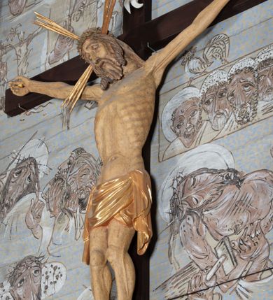 Zdjęcie nr 7: Figura Chrystusa przybita do krzyża trzema gwoździami pełna, niedrążona. Ciało w niewielkim zwisie, głowa delikatnie opada na prawy bark, stopy skrzyżowane w układzie prawa na lewą. Sylwetka podkreślona wydatną klatką piersiową, z wyraźnie zaznaczoną linią żeber i mostka, a także z precyzyjnie ukazaną anatomią. Twarz podłużna, z długim nosem, przymkniętymi oczami, okolona brodą ułożoną w długie, równolegle opadające, proste pukle. Włosy długie, brązowe, spływające na plecy oraz z przodu dwoma, silnie skręconymi lokami. Na głowie zielona korona cierniowa, a wokół niej nimb krzyżowy złożony z trzech wiązek promieni. Perizonium ciasno oplatające biodra, z dwoma zwisami po bokach, po lewej stronie dłuższym. Polichromia ciała naturalistyczna z delikatnie zaznaczonymi śladami męki, perizonium, gwoździe i nimb złocone. Nad głową Chrystusa titulus w formie pionowej banderoli z napisem „J[esus] N[azarenus] / R[ex] J[udaeorum]”.