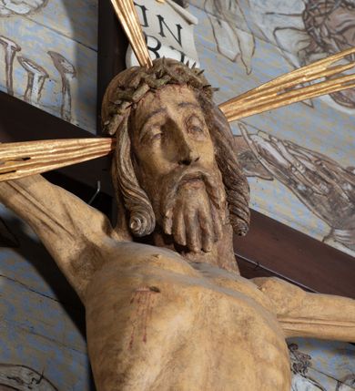 Zdjęcie nr 11: Figura Chrystusa przybita do krzyża trzema gwoździami pełna, niedrążona. Ciało w niewielkim zwisie, głowa delikatnie opada na prawy bark, stopy skrzyżowane w układzie prawa na lewą. Sylwetka podkreślona wydatną klatką piersiową, z wyraźnie zaznaczoną linią żeber i mostka, a także z precyzyjnie ukazaną anatomią. Twarz podłużna, z długim nosem, przymkniętymi oczami, okolona brodą ułożoną w długie, równolegle opadające, proste pukle. Włosy długie, brązowe, spływające na plecy oraz z przodu dwoma, silnie skręconymi lokami. Na głowie zielona korona cierniowa, a wokół niej nimb krzyżowy złożony z trzech wiązek promieni. Perizonium ciasno oplatające biodra, z dwoma zwisami po bokach, po lewej stronie dłuższym. Polichromia ciała naturalistyczna z delikatnie zaznaczonymi śladami męki, perizonium, gwoździe i nimb złocone. Nad głową Chrystusa titulus w formie pionowej banderoli z napisem „J[esus] N[azarenus] / R[ex] J[udaeorum]”.