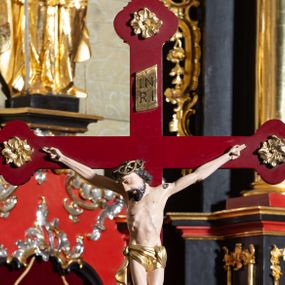 Zdjęcie nr 1: Rzeźba pełnoplastyczna, Chrystus przybity do krzyża trzema gwoździami. Figura w delikatnym zwisie, ramiona szeroko rozłożone, kolana delikatnie ugięte, stopy w układzie prawa na lewą. Twarz pociągła, szczupła, o długim nosie, oczy zamknięte, usta szerokie, rozchylone; okolona krótką brodą. Włosy półdługie, ułożone w skręcone pukle opadające na kark i prawe ramię. Na głowie korona cierniowa. Głowa nieproporcjonalnie duża w stosunku do ciała, sylwetka szczupła, z wyraźnie uwypuklonym umięśnieniem i linią żeber klatki piersiowej, z zaznaczonymi śladami męki. Perizonium w formie tkaniny ściśle owijającej biodra, zawiązanej na prawym boku ze zwisem z prawej strony. Nad głową Chrystusa złocony titulus w formie banderoli z napisem: „I(ESUS) N(AZARENUS) / R(EX) I(UDAEROUM)”. Krzyż gładki o trójlistnie zakończonych ramionach, zdobionych rozetkami, malowany na czerwono. Osadzony na podstawie zdobionej dwiema fantazyjnie wyciętymi deseczkami zdobionymi rzeźbionymi, złoconymi gałązkami róż. Podstawa umieszczona na niskim prostokątnym cokoliku na czterech płaskich nóżkach. Polichromia naturalistyczna w odsłoniętych partiach ciała, perizonium i korona złocone.