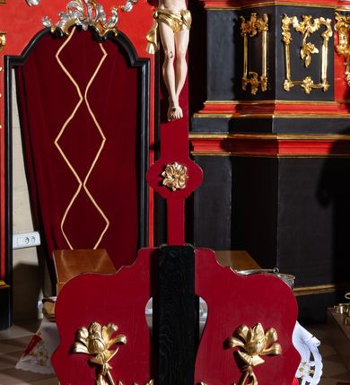 Zdjęcie nr 2: Rzeźba pełnoplastyczna, Chrystus przybity do krzyża trzema gwoździami. Figura w delikatnym zwisie, ramiona szeroko rozłożone, kolana delikatnie ugięte, stopy w układzie prawa na lewą. Twarz pociągła, szczupła, o długim nosie, oczy zamknięte, usta szerokie, rozchylone; okolona krótką brodą. Włosy półdługie, ułożone w skręcone pukle opadające na kark i prawe ramię. Na głowie korona cierniowa. Głowa nieproporcjonalnie duża w stosunku do ciała, sylwetka szczupła, z wyraźnie uwypuklonym umięśnieniem i linią żeber klatki piersiowej, z zaznaczonymi śladami męki. Perizonium w formie tkaniny ściśle owijającej biodra, zawiązanej na prawym boku ze zwisem z prawej strony. Nad głową Chrystusa złocony titulus w formie banderoli z napisem: „I(ESUS) N(AZARENUS) / R(EX) I(UDAEROUM)”. Krzyż gładki o trójlistnie zakończonych ramionach, zdobionych rozetkami, malowany na czerwono. Osadzony na podstawie zdobionej dwiema fantazyjnie wyciętymi deseczkami zdobionymi rzeźbionymi, złoconymi gałązkami róż. Podstawa umieszczona na niskim prostokątnym cokoliku na czterech płaskich nóżkach. Polichromia naturalistyczna w odsłoniętych partiach ciała, perizonium i korona złocone.