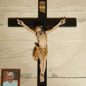 Zdjęcie nr 1: Rzeźba Chrystusa przybita do krzyża trzema gwoździami w głębokim zwisie na ramionach. Sylwetka szczupła o mocno podkreślonej, guzowatej linii żeber, z zaznaczonym mostkiem, kolana złączone, stopy założone w układzie prawa na lewą, ramiona delikatnie umięśnione, dwa palce u dłoni rozprostowane, głowa przechylona na prawe ramię. Twarz podłużna, okolona krótką brodą, usta delikatnie rozchylone, oczy przymknięte ze wzrokiem skierowanym w dół, nos długi i wąski. Włosy długie, ciemnobrązowe, opadają na plecy i dwoma puklami do przodu na ramiona, na głowie założona jest głęboko osadzona, złocona korona cierniowa. Perizonium złocone, zawiązane na guza na prawym boku i spływające łagodnymi falami wzdłuż prawego uda, z przodu układające się na kształt trójkątnej chusty. Z boku, dłoni, stóp i spod korony cierniowej spływają strużki krwi. Polichromia ciała naturalistyczna. Krzyż gładki, prosty, malowany na czarno; nad głową Chrystusa złocony titulus w formie pionowej banderoli z napisem „IN / RI”. Na krawędzi u nasady dolnej belki napis malowany białą farbą: „NS”. 
