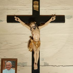 Zdjęcie nr 1: Rzeźba Chrystusa przybita do krzyża trzema gwoździami w głębokim zwisie na ramionach. Sylwetka szczupła o mocno podkreślonej, guzowatej linii żeber, z zaznaczonym mostkiem, kolana złączone, stopy założone w układzie prawa na lewą, ramiona delikatnie umięśnione, dwa palce u dłoni rozprostowane, głowa przechylona na prawe ramię. Twarz podłużna, okolona krótką brodą, usta delikatnie rozchylone, oczy przymknięte ze wzrokiem skierowanym w dół, nos długi i wąski. Włosy długie, ciemnobrązowe, opadają na plecy i dwoma puklami do przodu na ramiona, na głowie założona jest głęboko osadzona, złocona korona cierniowa. Perizonium złocone, zawiązane na guza na prawym boku i spływające łagodnymi falami wzdłuż prawego uda, z przodu układające się na kształt trójkątnej chusty. Z boku, dłoni, stóp i spod korony cierniowej spływają strużki krwi. Polichromia ciała naturalistyczna. Krzyż gładki, prosty, malowany na czarno; nad głową Chrystusa złocony titulus w formie pionowej banderoli z napisem „IN / RI”. Na krawędzi u nasady dolnej belki napis malowany białą farbą: „NS”. 
