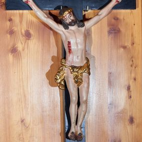 Zdjęcie nr 1: Rzeźba Chrystusa przybita do krzyża czterema gwoździami w głębokim zwisie na ramionach. Sylwetka szczupła o podkreślonej anatomii, głowa przechylona delikatnie na prawe ramię, dłonie silnie zaciśnięte, kolana rozdzielone, stopy złożone obok siebie, przebite oddzielnie. Twarz szczupła z szerokim, trójkątnym nosem, małymi oczami, okolona krótką brodą. Włosy długie, bujne i ciemnobrązowe, spływające na oba ramiona, rzeźbione w grube pasma; na głowie złocona korona cierniowa. Perizonium zawieszone na sznurze, z przodu z jednym końcem przewieszonym przez sznur, a z drugim zawiązanym na prawym boku, silnie drapowane. Z boku, dłoni, stóp i spod korony cierniowej spływają strużki krwi. Polichromia ciała naturalistyczna. Krzyż gładki, prosty i malowany na czarno; nad głową Chrystusa titulus w formie poziomej banderoli z napisem „I.N. / R.I.”. 
