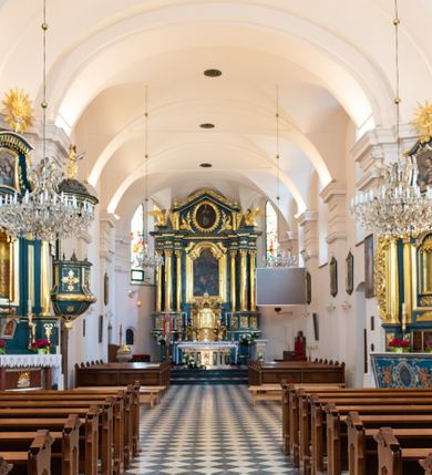 Zdjęcie nr 18: Kościół orientowany, jest budowlą murowaną z cegły i kamienia, na rzucie podłużnym. Korpus jednonawowy i trójprzęsłowy. Stosunkowo szerokie, trójprzęsłowe, zamknięte trójbocznie prezbiterium z przylegającą od północy zakrystią. Na osi kościoła przylega do fasady trójkondygnacyjna wieża z kruchtą w przyziemiu i przyległością od południa, w której mieszczą się prowadzące na wieżę schody.  Od południa i zachodu, na wysokości trzeciego przęsła do korpusu przylega kaplic na rzutach zbliżonych do kwadratów, z czego południową od wschodu i zachodu flankuje para krucht. Nawa, prezbiterium i kaplica północna przekryte są sklepieniami kolebkowymi z lunetami wspartymi na parach lub pojedynczych pilastrach. Kaplica południowa nakryta jest kopułą wspartą na 4 pendentywach. Artykulację ścian na zewnątrz korpusu nawowego i prezbiterium stanowi zespół przypór. Naroża kaplicy południowej ujmują zwielokrotnione pilastry wpierające obiegający bryłę gzyms wieńczący. Naroża kaplicy północnej ujmuje para neogotyckich przypór, natomiast północną ścianę wieńczy neogotycki szczyt schodkowy. 
Do wnętrza prowadzi 6 otworów drzwiowych – 1 w kruchcie w wieży ujęte kamienny, półkoliście zamkniętym portalem schodkowym z dwuskrzydłowymi drzwiami z nadświetlem, 1 zamknięte łukiem półkolistym w przyległości obok wieży, 3 w kruchtach flankujących kaplicę południową – z czego w zachodniej jedno w formie dużych dwuskrzydłowych drzwi z kwaterami bocznymi i nadświetlem, we wschodniej 2 ujęte prostokątnymi, kamiennymi portalami z wąskim nadświetlem i parą uszaków, zwieńczonych parą stykających się wolut z krzyżem na kuli w szczycie oraz 1 prowadzące do zakrystii. Okna korpusu nawowego i prezbiterium w kształcie stojących prostokątów zamkniętych półkoliście, z czego w prezbiterium są smukłe i wysokie. Okna kaplicy północnej zamknięte łukiem koszowym, natomiast kaplicy południowej w postaci prostokątów ujętych kamiennymi obramieniami z uszakami na narożach. 3 z 4 ścian wieży przeprute oknami, po 1 na każdej z kondygnacji, z czego na pierwszej zamknięte półkoliście, na drugiej w kształcie stojącego prostokąta i na trzeciej ostrołukowe. Wieżę wieńczy ceglany szczyt z wydzielonym gzymsami fryzem arkadkowym, wyżej 4 trójkątne szczyty umieszczone na osiach każdej ze ścian ujęte w narożach 4 małymi pinaklami i hełmem pośrodku w formie wysokiego pinakla. Korpus nawowy i prezbiterium przekrywa dach dwuspadowy, kryty blachą, z pinaklową wieżyczką na sygnaturkę na połączeniu tych przestrzeni, kaplicę południową kopuła z latarnią, przylegające do niej kruchty dachy pulpitowe, natomiast kaplica północna ma dach dwuspadowy. Otynkowane ściany kościoła są pomalowane w kolorze białym, miejscami pozostawiony kamienny mur.     
