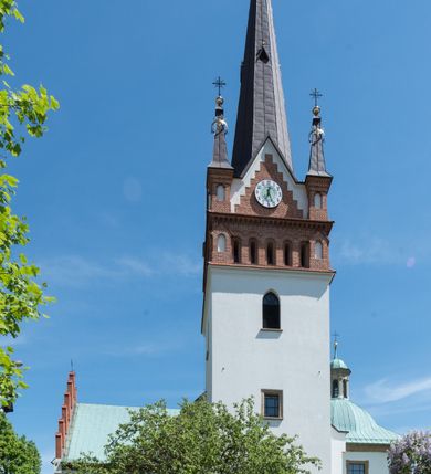 Zdjęcie nr 3: Kościół orientowany, jest budowlą murowaną z cegły i kamienia, na rzucie podłużnym. Korpus jednonawowy i trójprzęsłowy. Stosunkowo szerokie, trójprzęsłowe, zamknięte trójbocznie prezbiterium z przylegającą od północy zakrystią. Na osi kościoła przylega do fasady trójkondygnacyjna wieża z kruchtą w przyziemiu i przyległością od południa, w której mieszczą się prowadzące na wieżę schody.  Od południa i zachodu, na wysokości trzeciego przęsła do korpusu przylega kaplic na rzutach zbliżonych do kwadratów, z czego południową od wschodu i zachodu flankuje para krucht. Nawa, prezbiterium i kaplica północna przekryte są sklepieniami kolebkowymi z lunetami wspartymi na parach lub pojedynczych pilastrach. Kaplica południowa nakryta jest kopułą wspartą na 4 pendentywach. Artykulację ścian na zewnątrz korpusu nawowego i prezbiterium stanowi zespół przypór. Naroża kaplicy południowej ujmują zwielokrotnione pilastry wpierające obiegający bryłę gzyms wieńczący. Naroża kaplicy północnej ujmuje para neogotyckich przypór, natomiast północną ścianę wieńczy neogotycki szczyt schodkowy. 
Do wnętrza prowadzi 6 otworów drzwiowych – 1 w kruchcie w wieży ujęte kamienny, półkoliście zamkniętym portalem schodkowym z dwuskrzydłowymi drzwiami z nadświetlem, 1 zamknięte łukiem półkolistym w przyległości obok wieży, 3 w kruchtach flankujących kaplicę południową – z czego w zachodniej jedno w formie dużych dwuskrzydłowych drzwi z kwaterami bocznymi i nadświetlem, we wschodniej 2 ujęte prostokątnymi, kamiennymi portalami z wąskim nadświetlem i parą uszaków, zwieńczonych parą stykających się wolut z krzyżem na kuli w szczycie oraz 1 prowadzące do zakrystii. Okna korpusu nawowego i prezbiterium w kształcie stojących prostokątów zamkniętych półkoliście, z czego w prezbiterium są smukłe i wysokie. Okna kaplicy północnej zamknięte łukiem koszowym, natomiast kaplicy południowej w postaci prostokątów ujętych kamiennymi obramieniami z uszakami na narożach. 3 z 4 ścian wieży przeprute oknami, po 1 na każdej z kondygnacji, z czego na pierwszej zamknięte półkoliście, na drugiej w kształcie stojącego prostokąta i na trzeciej ostrołukowe. Wieżę wieńczy ceglany szczyt z wydzielonym gzymsami fryzem arkadkowym, wyżej 4 trójkątne szczyty umieszczone na osiach każdej ze ścian ujęte w narożach 4 małymi pinaklami i hełmem pośrodku w formie wysokiego pinakla. Korpus nawowy i prezbiterium przekrywa dach dwuspadowy, kryty blachą, z pinaklową wieżyczką na sygnaturkę na połączeniu tych przestrzeni, kaplicę południową kopuła z latarnią, przylegające do niej kruchty dachy pulpitowe, natomiast kaplica północna ma dach dwuspadowy. Otynkowane ściany kościoła są pomalowane w kolorze białym, miejscami pozostawiony kamienny mur.     
