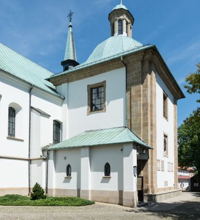 Zdjęcie nr 8: Kościół orientowany, jest budowlą murowaną z cegły i kamienia, na rzucie podłużnym. Korpus jednonawowy i trójprzęsłowy. Stosunkowo szerokie, trójprzęsłowe, zamknięte trójbocznie prezbiterium z przylegającą od północy zakrystią. Na osi kościoła przylega do fasady trójkondygnacyjna wieża z kruchtą w przyziemiu i przyległością od południa, w której mieszczą się prowadzące na wieżę schody.  Od południa i zachodu, na wysokości trzeciego przęsła do korpusu przylega kaplic na rzutach zbliżonych do kwadratów, z czego południową od wschodu i zachodu flankuje para krucht. Nawa, prezbiterium i kaplica północna przekryte są sklepieniami kolebkowymi z lunetami wspartymi na parach lub pojedynczych pilastrach. Kaplica południowa nakryta jest kopułą wspartą na 4 pendentywach. Artykulację ścian na zewnątrz korpusu nawowego i prezbiterium stanowi zespół przypór. Naroża kaplicy południowej ujmują zwielokrotnione pilastry wpierające obiegający bryłę gzyms wieńczący. Naroża kaplicy północnej ujmuje para neogotyckich przypór, natomiast północną ścianę wieńczy neogotycki szczyt schodkowy. 
Do wnętrza prowadzi 6 otworów drzwiowych – 1 w kruchcie w wieży ujęte kamienny, półkoliście zamkniętym portalem schodkowym z dwuskrzydłowymi drzwiami z nadświetlem, 1 zamknięte łukiem półkolistym w przyległości obok wieży, 3 w kruchtach flankujących kaplicę południową – z czego w zachodniej jedno w formie dużych dwuskrzydłowych drzwi z kwaterami bocznymi i nadświetlem, we wschodniej 2 ujęte prostokątnymi, kamiennymi portalami z wąskim nadświetlem i parą uszaków, zwieńczonych parą stykających się wolut z krzyżem na kuli w szczycie oraz 1 prowadzące do zakrystii. Okna korpusu nawowego i prezbiterium w kształcie stojących prostokątów zamkniętych półkoliście, z czego w prezbiterium są smukłe i wysokie. Okna kaplicy północnej zamknięte łukiem koszowym, natomiast kaplicy południowej w postaci prostokątów ujętych kamiennymi obramieniami z uszakami na narożach. 3 z 4 ścian wieży przeprute oknami, po 1 na każdej z kondygnacji, z czego na pierwszej zamknięte półkoliście, na drugiej w kształcie stojącego prostokąta i na trzeciej ostrołukowe. Wieżę wieńczy ceglany szczyt z wydzielonym gzymsami fryzem arkadkowym, wyżej 4 trójkątne szczyty umieszczone na osiach każdej ze ścian ujęte w narożach 4 małymi pinaklami i hełmem pośrodku w formie wysokiego pinakla. Korpus nawowy i prezbiterium przekrywa dach dwuspadowy, kryty blachą, z pinaklową wieżyczką na sygnaturkę na połączeniu tych przestrzeni, kaplicę południową kopuła z latarnią, przylegające do niej kruchty dachy pulpitowe, natomiast kaplica północna ma dach dwuspadowy. Otynkowane ściany kościoła są pomalowane w kolorze białym, miejscami pozostawiony kamienny mur.     
