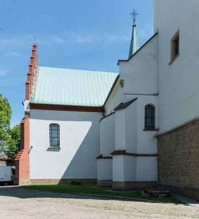 Zdjęcie nr 12: Kościół orientowany, jest budowlą murowaną z cegły i kamienia, na rzucie podłużnym. Korpus jednonawowy i trójprzęsłowy. Stosunkowo szerokie, trójprzęsłowe, zamknięte trójbocznie prezbiterium z przylegającą od północy zakrystią. Na osi kościoła przylega do fasady trójkondygnacyjna wieża z kruchtą w przyziemiu i przyległością od południa, w której mieszczą się prowadzące na wieżę schody.  Od południa i zachodu, na wysokości trzeciego przęsła do korpusu przylega kaplic na rzutach zbliżonych do kwadratów, z czego południową od wschodu i zachodu flankuje para krucht. Nawa, prezbiterium i kaplica północna przekryte są sklepieniami kolebkowymi z lunetami wspartymi na parach lub pojedynczych pilastrach. Kaplica południowa nakryta jest kopułą wspartą na 4 pendentywach. Artykulację ścian na zewnątrz korpusu nawowego i prezbiterium stanowi zespół przypór. Naroża kaplicy południowej ujmują zwielokrotnione pilastry wpierające obiegający bryłę gzyms wieńczący. Naroża kaplicy północnej ujmuje para neogotyckich przypór, natomiast północną ścianę wieńczy neogotycki szczyt schodkowy. 
Do wnętrza prowadzi 6 otworów drzwiowych – 1 w kruchcie w wieży ujęte kamienny, półkoliście zamkniętym portalem schodkowym z dwuskrzydłowymi drzwiami z nadświetlem, 1 zamknięte łukiem półkolistym w przyległości obok wieży, 3 w kruchtach flankujących kaplicę południową – z czego w zachodniej jedno w formie dużych dwuskrzydłowych drzwi z kwaterami bocznymi i nadświetlem, we wschodniej 2 ujęte prostokątnymi, kamiennymi portalami z wąskim nadświetlem i parą uszaków, zwieńczonych parą stykających się wolut z krzyżem na kuli w szczycie oraz 1 prowadzące do zakrystii. Okna korpusu nawowego i prezbiterium w kształcie stojących prostokątów zamkniętych półkoliście, z czego w prezbiterium są smukłe i wysokie. Okna kaplicy północnej zamknięte łukiem koszowym, natomiast kaplicy południowej w postaci prostokątów ujętych kamiennymi obramieniami z uszakami na narożach. 3 z 4 ścian wieży przeprute oknami, po 1 na każdej z kondygnacji, z czego na pierwszej zamknięte półkoliście, na drugiej w kształcie stojącego prostokąta i na trzeciej ostrołukowe. Wieżę wieńczy ceglany szczyt z wydzielonym gzymsami fryzem arkadkowym, wyżej 4 trójkątne szczyty umieszczone na osiach każdej ze ścian ujęte w narożach 4 małymi pinaklami i hełmem pośrodku w formie wysokiego pinakla. Korpus nawowy i prezbiterium przekrywa dach dwuspadowy, kryty blachą, z pinaklową wieżyczką na sygnaturkę na połączeniu tych przestrzeni, kaplicę południową kopuła z latarnią, przylegające do niej kruchty dachy pulpitowe, natomiast kaplica północna ma dach dwuspadowy. Otynkowane ściany kościoła są pomalowane w kolorze białym, miejscami pozostawiony kamienny mur.     
