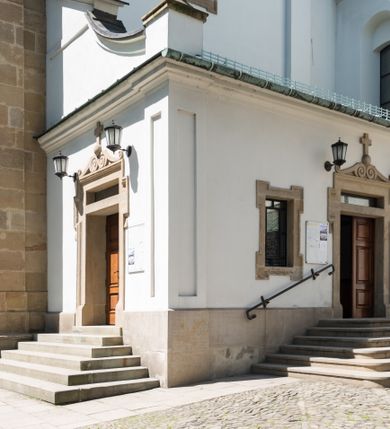 Zdjęcie nr 10: Kościół orientowany, jest budowlą murowaną z cegły i kamienia, na rzucie podłużnym. Korpus jednonawowy i trójprzęsłowy. Stosunkowo szerokie, trójprzęsłowe, zamknięte trójbocznie prezbiterium z przylegającą od północy zakrystią. Na osi kościoła przylega do fasady trójkondygnacyjna wieża z kruchtą w przyziemiu i przyległością od południa, w której mieszczą się prowadzące na wieżę schody.  Od południa i zachodu, na wysokości trzeciego przęsła do korpusu przylega kaplic na rzutach zbliżonych do kwadratów, z czego południową od wschodu i zachodu flankuje para krucht. Nawa, prezbiterium i kaplica północna przekryte są sklepieniami kolebkowymi z lunetami wspartymi na parach lub pojedynczych pilastrach. Kaplica południowa nakryta jest kopułą wspartą na 4 pendentywach. Artykulację ścian na zewnątrz korpusu nawowego i prezbiterium stanowi zespół przypór. Naroża kaplicy południowej ujmują zwielokrotnione pilastry wpierające obiegający bryłę gzyms wieńczący. Naroża kaplicy północnej ujmuje para neogotyckich przypór, natomiast północną ścianę wieńczy neogotycki szczyt schodkowy. 
Do wnętrza prowadzi 6 otworów drzwiowych – 1 w kruchcie w wieży ujęte kamienny, półkoliście zamkniętym portalem schodkowym z dwuskrzydłowymi drzwiami z nadświetlem, 1 zamknięte łukiem półkolistym w przyległości obok wieży, 3 w kruchtach flankujących kaplicę południową – z czego w zachodniej jedno w formie dużych dwuskrzydłowych drzwi z kwaterami bocznymi i nadświetlem, we wschodniej 2 ujęte prostokątnymi, kamiennymi portalami z wąskim nadświetlem i parą uszaków, zwieńczonych parą stykających się wolut z krzyżem na kuli w szczycie oraz 1 prowadzące do zakrystii. Okna korpusu nawowego i prezbiterium w kształcie stojących prostokątów zamkniętych półkoliście, z czego w prezbiterium są smukłe i wysokie. Okna kaplicy północnej zamknięte łukiem koszowym, natomiast kaplicy południowej w postaci prostokątów ujętych kamiennymi obramieniami z uszakami na narożach. 3 z 4 ścian wieży przeprute oknami, po 1 na każdej z kondygnacji, z czego na pierwszej zamknięte półkoliście, na drugiej w kształcie stojącego prostokąta i na trzeciej ostrołukowe. Wieżę wieńczy ceglany szczyt z wydzielonym gzymsami fryzem arkadkowym, wyżej 4 trójkątne szczyty umieszczone na osiach każdej ze ścian ujęte w narożach 4 małymi pinaklami i hełmem pośrodku w formie wysokiego pinakla. Korpus nawowy i prezbiterium przekrywa dach dwuspadowy, kryty blachą, z pinaklową wieżyczką na sygnaturkę na połączeniu tych przestrzeni, kaplicę południową kopuła z latarnią, przylegające do niej kruchty dachy pulpitowe, natomiast kaplica północna ma dach dwuspadowy. Otynkowane ściany kościoła są pomalowane w kolorze białym, miejscami pozostawiony kamienny mur.     
