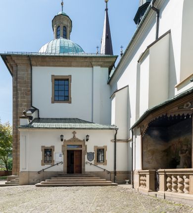 Zdjęcie nr 11: Kościół orientowany, jest budowlą murowaną z cegły i kamienia, na rzucie podłużnym. Korpus jednonawowy i trójprzęsłowy. Stosunkowo szerokie, trójprzęsłowe, zamknięte trójbocznie prezbiterium z przylegającą od północy zakrystią. Na osi kościoła przylega do fasady trójkondygnacyjna wieża z kruchtą w przyziemiu i przyległością od południa, w której mieszczą się prowadzące na wieżę schody.  Od południa i zachodu, na wysokości trzeciego przęsła do korpusu przylega kaplic na rzutach zbliżonych do kwadratów, z czego południową od wschodu i zachodu flankuje para krucht. Nawa, prezbiterium i kaplica północna przekryte są sklepieniami kolebkowymi z lunetami wspartymi na parach lub pojedynczych pilastrach. Kaplica południowa nakryta jest kopułą wspartą na 4 pendentywach. Artykulację ścian na zewnątrz korpusu nawowego i prezbiterium stanowi zespół przypór. Naroża kaplicy południowej ujmują zwielokrotnione pilastry wpierające obiegający bryłę gzyms wieńczący. Naroża kaplicy północnej ujmuje para neogotyckich przypór, natomiast północną ścianę wieńczy neogotycki szczyt schodkowy. 
Do wnętrza prowadzi 6 otworów drzwiowych – 1 w kruchcie w wieży ujęte kamienny, półkoliście zamkniętym portalem schodkowym z dwuskrzydłowymi drzwiami z nadświetlem, 1 zamknięte łukiem półkolistym w przyległości obok wieży, 3 w kruchtach flankujących kaplicę południową – z czego w zachodniej jedno w formie dużych dwuskrzydłowych drzwi z kwaterami bocznymi i nadświetlem, we wschodniej 2 ujęte prostokątnymi, kamiennymi portalami z wąskim nadświetlem i parą uszaków, zwieńczonych parą stykających się wolut z krzyżem na kuli w szczycie oraz 1 prowadzące do zakrystii. Okna korpusu nawowego i prezbiterium w kształcie stojących prostokątów zamkniętych półkoliście, z czego w prezbiterium są smukłe i wysokie. Okna kaplicy północnej zamknięte łukiem koszowym, natomiast kaplicy południowej w postaci prostokątów ujętych kamiennymi obramieniami z uszakami na narożach. 3 z 4 ścian wieży przeprute oknami, po 1 na każdej z kondygnacji, z czego na pierwszej zamknięte półkoliście, na drugiej w kształcie stojącego prostokąta i na trzeciej ostrołukowe. Wieżę wieńczy ceglany szczyt z wydzielonym gzymsami fryzem arkadkowym, wyżej 4 trójkątne szczyty umieszczone na osiach każdej ze ścian ujęte w narożach 4 małymi pinaklami i hełmem pośrodku w formie wysokiego pinakla. Korpus nawowy i prezbiterium przekrywa dach dwuspadowy, kryty blachą, z pinaklową wieżyczką na sygnaturkę na połączeniu tych przestrzeni, kaplicę południową kopuła z latarnią, przylegające do niej kruchty dachy pulpitowe, natomiast kaplica północna ma dach dwuspadowy. Otynkowane ściany kościoła są pomalowane w kolorze białym, miejscami pozostawiony kamienny mur.     
