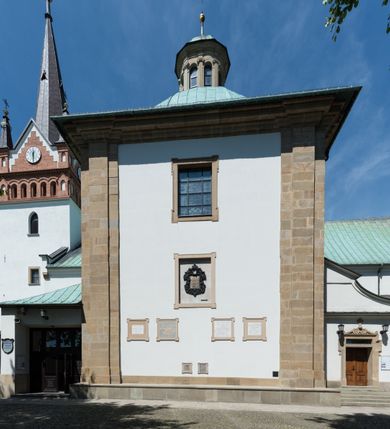 Zdjęcie nr 7: Kościół orientowany, jest budowlą murowaną z cegły i kamienia, na rzucie podłużnym. Korpus jednonawowy i trójprzęsłowy. Stosunkowo szerokie, trójprzęsłowe, zamknięte trójbocznie prezbiterium z przylegającą od północy zakrystią. Na osi kościoła przylega do fasady trójkondygnacyjna wieża z kruchtą w przyziemiu i przyległością od południa, w której mieszczą się prowadzące na wieżę schody.  Od południa i zachodu, na wysokości trzeciego przęsła do korpusu przylega kaplic na rzutach zbliżonych do kwadratów, z czego południową od wschodu i zachodu flankuje para krucht. Nawa, prezbiterium i kaplica północna przekryte są sklepieniami kolebkowymi z lunetami wspartymi na parach lub pojedynczych pilastrach. Kaplica południowa nakryta jest kopułą wspartą na 4 pendentywach. Artykulację ścian na zewnątrz korpusu nawowego i prezbiterium stanowi zespół przypór. Naroża kaplicy południowej ujmują zwielokrotnione pilastry wpierające obiegający bryłę gzyms wieńczący. Naroża kaplicy północnej ujmuje para neogotyckich przypór, natomiast północną ścianę wieńczy neogotycki szczyt schodkowy. 
Do wnętrza prowadzi 6 otworów drzwiowych – 1 w kruchcie w wieży ujęte kamienny, półkoliście zamkniętym portalem schodkowym z dwuskrzydłowymi drzwiami z nadświetlem, 1 zamknięte łukiem półkolistym w przyległości obok wieży, 3 w kruchtach flankujących kaplicę południową – z czego w zachodniej jedno w formie dużych dwuskrzydłowych drzwi z kwaterami bocznymi i nadświetlem, we wschodniej 2 ujęte prostokątnymi, kamiennymi portalami z wąskim nadświetlem i parą uszaków, zwieńczonych parą stykających się wolut z krzyżem na kuli w szczycie oraz 1 prowadzące do zakrystii. Okna korpusu nawowego i prezbiterium w kształcie stojących prostokątów zamkniętych półkoliście, z czego w prezbiterium są smukłe i wysokie. Okna kaplicy północnej zamknięte łukiem koszowym, natomiast kaplicy południowej w postaci prostokątów ujętych kamiennymi obramieniami z uszakami na narożach. 3 z 4 ścian wieży przeprute oknami, po 1 na każdej z kondygnacji, z czego na pierwszej zamknięte półkoliście, na drugiej w kształcie stojącego prostokąta i na trzeciej ostrołukowe. Wieżę wieńczy ceglany szczyt z wydzielonym gzymsami fryzem arkadkowym, wyżej 4 trójkątne szczyty umieszczone na osiach każdej ze ścian ujęte w narożach 4 małymi pinaklami i hełmem pośrodku w formie wysokiego pinakla. Korpus nawowy i prezbiterium przekrywa dach dwuspadowy, kryty blachą, z pinaklową wieżyczką na sygnaturkę na połączeniu tych przestrzeni, kaplicę południową kopuła z latarnią, przylegające do niej kruchty dachy pulpitowe, natomiast kaplica północna ma dach dwuspadowy. Otynkowane ściany kościoła są pomalowane w kolorze białym, miejscami pozostawiony kamienny mur.     
