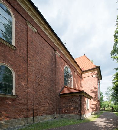 Zdjęcie nr 10: Kościół jest położony w centrum wsi, na południe od głównej drogi, na placu otoczonym płotem na kamiennej podmurówce. Wejście na plac kościelny prowadzi przez główną bramę od zachodu oraz drugą od północnego-wschodu. Kościół jest budowlą założoną na planie krzyża łacińskiego, murowaną, orientowaną z delikatnym odchyleniem ku południowi, jednonawową z transeptem, z prezbiterium zamkniętym trójbocznie, przy którym od północy jest zakrystia z emporą, a od południa kaplica. Wnętrze nawy głównej artykułowe jest dwiema płytkimi wnękami, zakończonymi półkoliście, w których w górnej części umieszczone są trójdzielne okna z maswerkami i witrażami. W prezbiterium i kaplicy sklepienie krzyżowo-żebrowe, w nawie gwieździste bez żeber. Nawę od prezbiterium oraz ramion transeptu oddzielają półkoliście zamknięte arkady. Na ścianie arkady tęczowej napis: „CHWAŁA CI TRÓJCO ŚWIĘTA”. W ramionach transeptu pojedyncze okna prostokątne, zamknięte półkoliście. Kolejne dwa okna, lecz węższe znajdują się w prezbiterium. 

Fasada dwukondygnacyjna z dostawioną wieżą na planie kwadratu. W dolnej kondygnacji fasada artykułowana parą pilastrów w narożach, podtrzymujących profilowany gzyms. Pośrodku główne wejście do kościoła zaakcentowane schodami i monumentalnym portalem z wimpergą i masywnymi kamiennymi węgarami. W górnej kondygnacji fasady uwidoczniona sylwetka wieży z każdej strony flankowana w narożach parą lizen podtrzymujących niepełne belkowanie i trójkątne przyczółki. Od frontu, po bokach wieży spływy wolutowe, w polu półkoliście zamknięte okno, a nad nim okrągłe. Na ścianach bocznych wieży analogiczne oculusy. Na szczycie wieży wysoka iglica. Pozostałe ściany kościoła artykułowe pilastrami, podtrzymującymi niepełne belkowanie zamknięte gzymsem podokapowym. Dach dwuspadowy, nakryty dachówką.

