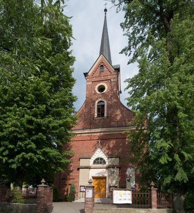 Zdjęcie nr 1: Kościół jest położony w centrum wsi, na południe od głównej drogi, na placu otoczonym płotem na kamiennej podmurówce. Wejście na plac kościelny prowadzi przez główną bramę od zachodu oraz drugą od północnego-wschodu. Kościół jest budowlą założoną na planie krzyża łacińskiego, murowaną, orientowaną z delikatnym odchyleniem ku południowi, jednonawową z transeptem, z prezbiterium zamkniętym trójbocznie, przy którym od północy jest zakrystia z emporą, a od południa kaplica. Wnętrze nawy głównej artykułowe jest dwiema płytkimi wnękami, zakończonymi półkoliście, w których w górnej części umieszczone są trójdzielne okna z maswerkami i witrażami. W prezbiterium i kaplicy sklepienie krzyżowo-żebrowe, w nawie gwieździste bez żeber. Nawę od prezbiterium oraz ramion transeptu oddzielają półkoliście zamknięte arkady. Na ścianie arkady tęczowej napis: „CHWAŁA CI TRÓJCO ŚWIĘTA”. W ramionach transeptu pojedyncze okna prostokątne, zamknięte półkoliście. Kolejne dwa okna, lecz węższe znajdują się w prezbiterium. 

Fasada dwukondygnacyjna z dostawioną wieżą na planie kwadratu. W dolnej kondygnacji fasada artykułowana parą pilastrów w narożach, podtrzymujących profilowany gzyms. Pośrodku główne wejście do kościoła zaakcentowane schodami i monumentalnym portalem z wimpergą i masywnymi kamiennymi węgarami. W górnej kondygnacji fasady uwidoczniona sylwetka wieży z każdej strony flankowana w narożach parą lizen podtrzymujących niepełne belkowanie i trójkątne przyczółki. Od frontu, po bokach wieży spływy wolutowe, w polu półkoliście zamknięte okno, a nad nim okrągłe. Na ścianach bocznych wieży analogiczne oculusy. Na szczycie wieży wysoka iglica. Pozostałe ściany kościoła artykułowe pilastrami, podtrzymującymi niepełne belkowanie zamknięte gzymsem podokapowym. Dach dwuspadowy, nakryty dachówką.

