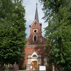 Zdjęcie nr 1: Kościół jest położony w centrum wsi, na południe od głównej drogi, na placu otoczonym płotem na kamiennej podmurówce. Wejście na plac kościelny prowadzi przez główną bramę od zachodu oraz drugą od północnego-wschodu. Kościół jest budowlą założoną na planie krzyża łacińskiego, murowaną, orientowaną z delikatnym odchyleniem ku południowi, jednonawową z transeptem, z prezbiterium zamkniętym trójbocznie, przy którym od północy jest zakrystia z emporą, a od południa kaplica. Wnętrze nawy głównej artykułowe jest dwiema płytkimi wnękami, zakończonymi półkoliście, w których w górnej części umieszczone są trójdzielne okna z maswerkami i witrażami. W prezbiterium i kaplicy sklepienie krzyżowo-żebrowe, w nawie gwieździste bez żeber. Nawę od prezbiterium oraz ramion transeptu oddzielają półkoliście zamknięte arkady. Na ścianie arkady tęczowej napis: „CHWAŁA CI TRÓJCO ŚWIĘTA”. W ramionach transeptu pojedyncze okna prostokątne, zamknięte półkoliście. Kolejne dwa okna, lecz węższe znajdują się w prezbiterium. 

Fasada dwukondygnacyjna z dostawioną wieżą na planie kwadratu. W dolnej kondygnacji fasada artykułowana parą pilastrów w narożach, podtrzymujących profilowany gzyms. Pośrodku główne wejście do kościoła zaakcentowane schodami i monumentalnym portalem z wimpergą i masywnymi kamiennymi węgarami. W górnej kondygnacji fasady uwidoczniona sylwetka wieży z każdej strony flankowana w narożach parą lizen podtrzymujących niepełne belkowanie i trójkątne przyczółki. Od frontu, po bokach wieży spływy wolutowe, w polu półkoliście zamknięte okno, a nad nim okrągłe. Na ścianach bocznych wieży analogiczne oculusy. Na szczycie wieży wysoka iglica. Pozostałe ściany kościoła artykułowe pilastrami, podtrzymującymi niepełne belkowanie zamknięte gzymsem podokapowym. Dach dwuspadowy, nakryty dachówką.

