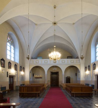 Zdjęcie nr 6: Kościół jest położony w centrum wsi, na południe od głównej drogi, na placu otoczonym płotem na kamiennej podmurówce. Wejście na plac kościelny prowadzi przez główną bramę od zachodu oraz drugą od północnego-wschodu. Kościół jest budowlą założoną na planie krzyża łacińskiego, murowaną, orientowaną z delikatnym odchyleniem ku południowi, jednonawową z transeptem, z prezbiterium zamkniętym trójbocznie, przy którym od północy jest zakrystia z emporą, a od południa kaplica. Wnętrze nawy głównej artykułowe jest dwiema płytkimi wnękami, zakończonymi półkoliście, w których w górnej części umieszczone są trójdzielne okna z maswerkami i witrażami. W prezbiterium i kaplicy sklepienie krzyżowo-żebrowe, w nawie gwieździste bez żeber. Nawę od prezbiterium oraz ramion transeptu oddzielają półkoliście zamknięte arkady. Na ścianie arkady tęczowej napis: „CHWAŁA CI TRÓJCO ŚWIĘTA”. W ramionach transeptu pojedyncze okna prostokątne, zamknięte półkoliście. Kolejne dwa okna, lecz węższe znajdują się w prezbiterium. 

Fasada dwukondygnacyjna z dostawioną wieżą na planie kwadratu. W dolnej kondygnacji fasada artykułowana parą pilastrów w narożach, podtrzymujących profilowany gzyms. Pośrodku główne wejście do kościoła zaakcentowane schodami i monumentalnym portalem z wimpergą i masywnymi kamiennymi węgarami. W górnej kondygnacji fasady uwidoczniona sylwetka wieży z każdej strony flankowana w narożach parą lizen podtrzymujących niepełne belkowanie i trójkątne przyczółki. Od frontu, po bokach wieży spływy wolutowe, w polu półkoliście zamknięte okno, a nad nim okrągłe. Na ścianach bocznych wieży analogiczne oculusy. Na szczycie wieży wysoka iglica. Pozostałe ściany kościoła artykułowe pilastrami, podtrzymującymi niepełne belkowanie zamknięte gzymsem podokapowym. Dach dwuspadowy, nakryty dachówką.

