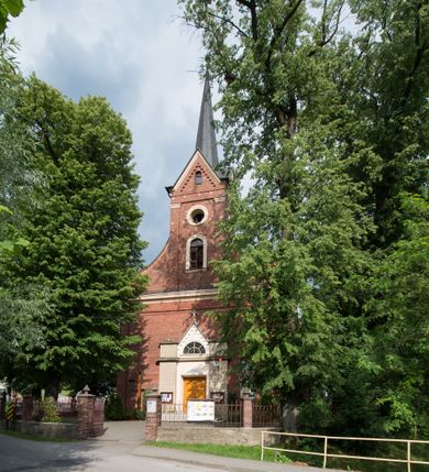 Zdjęcie nr 2: Kościół jest położony w centrum wsi, na południe od głównej drogi, na placu otoczonym płotem na kamiennej podmurówce. Wejście na plac kościelny prowadzi przez główną bramę od zachodu oraz drugą od północnego-wschodu. Kościół jest budowlą założoną na planie krzyża łacińskiego, murowaną, orientowaną z delikatnym odchyleniem ku południowi, jednonawową z transeptem, z prezbiterium zamkniętym trójbocznie, przy którym od północy jest zakrystia z emporą, a od południa kaplica. Wnętrze nawy głównej artykułowe jest dwiema płytkimi wnękami, zakończonymi półkoliście, w których w górnej części umieszczone są trójdzielne okna z maswerkami i witrażami. W prezbiterium i kaplicy sklepienie krzyżowo-żebrowe, w nawie gwieździste bez żeber. Nawę od prezbiterium oraz ramion transeptu oddzielają półkoliście zamknięte arkady. Na ścianie arkady tęczowej napis: „CHWAŁA CI TRÓJCO ŚWIĘTA”. W ramionach transeptu pojedyncze okna prostokątne, zamknięte półkoliście. Kolejne dwa okna, lecz węższe znajdują się w prezbiterium. 

Fasada dwukondygnacyjna z dostawioną wieżą na planie kwadratu. W dolnej kondygnacji fasada artykułowana parą pilastrów w narożach, podtrzymujących profilowany gzyms. Pośrodku główne wejście do kościoła zaakcentowane schodami i monumentalnym portalem z wimpergą i masywnymi kamiennymi węgarami. W górnej kondygnacji fasady uwidoczniona sylwetka wieży z każdej strony flankowana w narożach parą lizen podtrzymujących niepełne belkowanie i trójkątne przyczółki. Od frontu, po bokach wieży spływy wolutowe, w polu półkoliście zamknięte okno, a nad nim okrągłe. Na ścianach bocznych wieży analogiczne oculusy. Na szczycie wieży wysoka iglica. Pozostałe ściany kościoła artykułowe pilastrami, podtrzymującymi niepełne belkowanie zamknięte gzymsem podokapowym. Dach dwuspadowy, nakryty dachówką.

