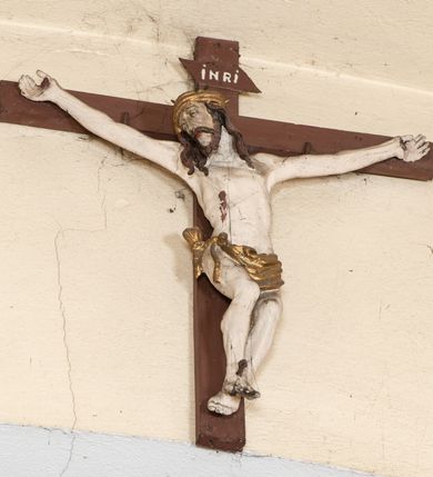 Zdjęcie nr 2: Rzeźba pełna. Figura Chrystusa ukazanego w niewielkim zwisie, o szeroko rozłożonych, niemal prostych ramionach, głowa uniesiona i przechylona na prawy bok, nogi ugięte w kolanach, stopy przebite jednym gwoździem w układzie prawa na lewą. Twarz pociągła, okolona zarostem, z długim i wąskim nosem, z częściowo otwartymi oczami. Włosy długie opadające na ramiona w postaci silnie skręconych pukli. Ciało o niewłaściwych proporcjach, umownie zarysowanej klatce piersiowej. Na głowie korona cierniowa w formie kołpaka. Perizonium z pasa tkaniny, krótkie, obficie i płasko drapowane, zawieszone na sznurze, z końcem przewiązanym na prawym boku. Polichromia karnacji widocznej w odsłoniętych partiach ciała naturalistyczna, korona i perizonium złocone. Na zakończeniu górnej belki krzyża titulus z napisem „INRI”, białym na brązowym tle. Krzyż prosty malowany na kolor brązowy. 
