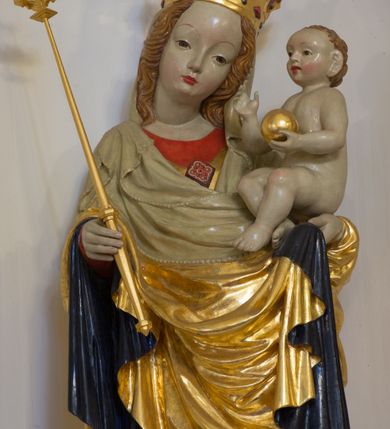 Zdjęcie nr 3: Rzeźba pełnoplastyczna, wolnostojąca, ukazująca Matkę Boską z Dzieciątkiem. Maria ustawiona frontalnie, w kontrapoście o sylwetce wygiętej na kształt litery „S”, z głową przechyloną na lewo. Na lewym ręku trzyma Dzieciątko i podtrzymuje dłonią płaszcz, w prawej dzierży berło. Twarz okrągła z wysokim czołem, drobnymi ustami i małymi oczami, o delikatnie zarysowanych łukach brwiowych. Włosy jasne, ułożone w skręcone pukle spływające na plecy. Madonna ubrana jest w czerwoną suknię, złoty płaszcz z ciemnogranatową podszewką spięty na piersi broszą w kształcie rombu oraz czarne buty. Na głowie ma założony beżowy welon spływający na ramiona i piersi oraz złotą koronę w typie otwartym, kameryzowaną. Draperia szat miękka o wyraźnie zaznaczonych, licznych fałdach misowych i kaskadowych. Dzieciątko ukazane w pozycji siedzącej, zwrócone w prawo, z nóżkami skrzyżowanymi, założonymi lewa na prawą. W lewej dłoni trzyma jabłko królewskie, a prawą podnosi do gestu błogosławieństwa. Twarz o dziecięcych rysach, z wysokim i wypukłym czołem, z delikatnie otwartymi ustami, okolona krótkimi i kędzierzawymi włosami. Polichromia w odsłoniętych partiach ciała o delikatnych odcieniach szarości, płaszcz i atrybuty złocone. 