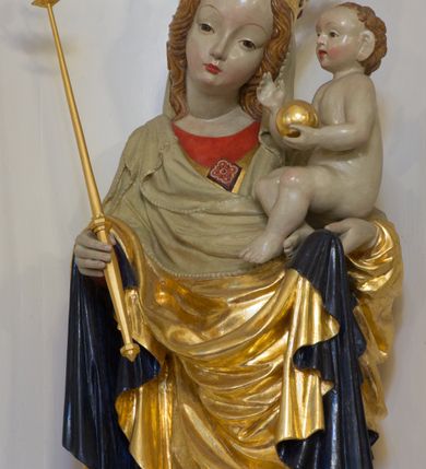 Zdjęcie nr 4: Rzeźba pełnoplastyczna, wolnostojąca, ukazująca Matkę Boską z Dzieciątkiem. Maria ustawiona frontalnie, w kontrapoście o sylwetce wygiętej na kształt litery „S”, z głową przechyloną na lewo. Na lewym ręku trzyma Dzieciątko i podtrzymuje dłonią płaszcz, w prawej dzierży berło. Twarz okrągła z wysokim czołem, drobnymi ustami i małymi oczami, o delikatnie zarysowanych łukach brwiowych. Włosy jasne, ułożone w skręcone pukle spływające na plecy. Madonna ubrana jest w czerwoną suknię, złoty płaszcz z ciemnogranatową podszewką spięty na piersi broszą w kształcie rombu oraz czarne buty. Na głowie ma założony beżowy welon spływający na ramiona i piersi oraz złotą koronę w typie otwartym, kameryzowaną. Draperia szat miękka o wyraźnie zaznaczonych, licznych fałdach misowych i kaskadowych. Dzieciątko ukazane w pozycji siedzącej, zwrócone w prawo, z nóżkami skrzyżowanymi, założonymi lewa na prawą. W lewej dłoni trzyma jabłko królewskie, a prawą podnosi do gestu błogosławieństwa. Twarz o dziecięcych rysach, z wysokim i wypukłym czołem, z delikatnie otwartymi ustami, okolona krótkimi i kędzierzawymi włosami. Polichromia w odsłoniętych partiach ciała o delikatnych odcieniach szarości, płaszcz i atrybuty złocone. 